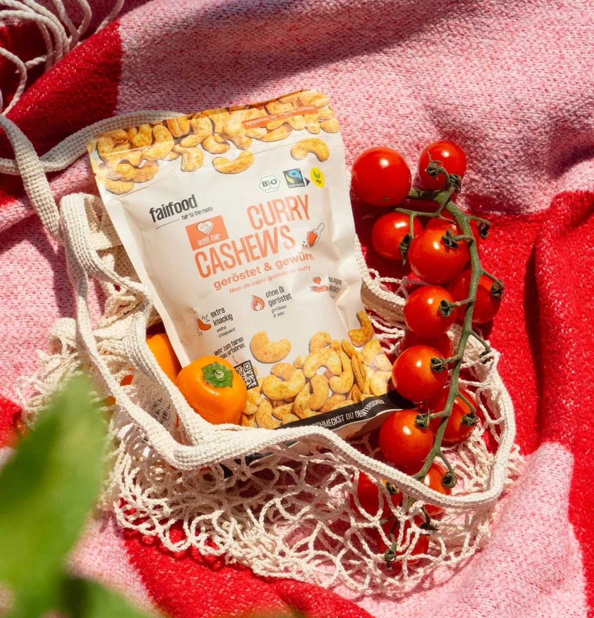 Beutel Curry Cashew und frische Tomaten liegen in Einkaufstasche auf Strandtuch