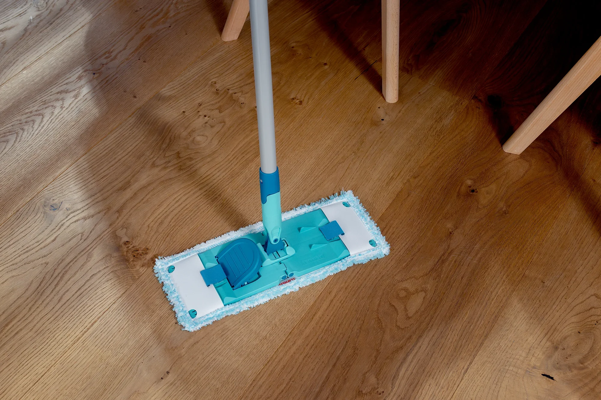 A POWER CLEAN floor mop is being used on a wooden floor. The mop has a blue handle and a rectangular mop head that efficiently removes dirt.