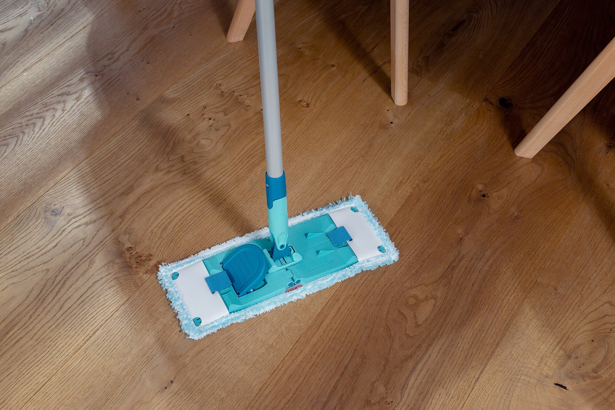 Een POWER CLEAN dweil wordt gebruikt op een houten vloer. De mop heeft een blauwe steel en een rechthoekige doek die efficiënt vuil verwijdert.