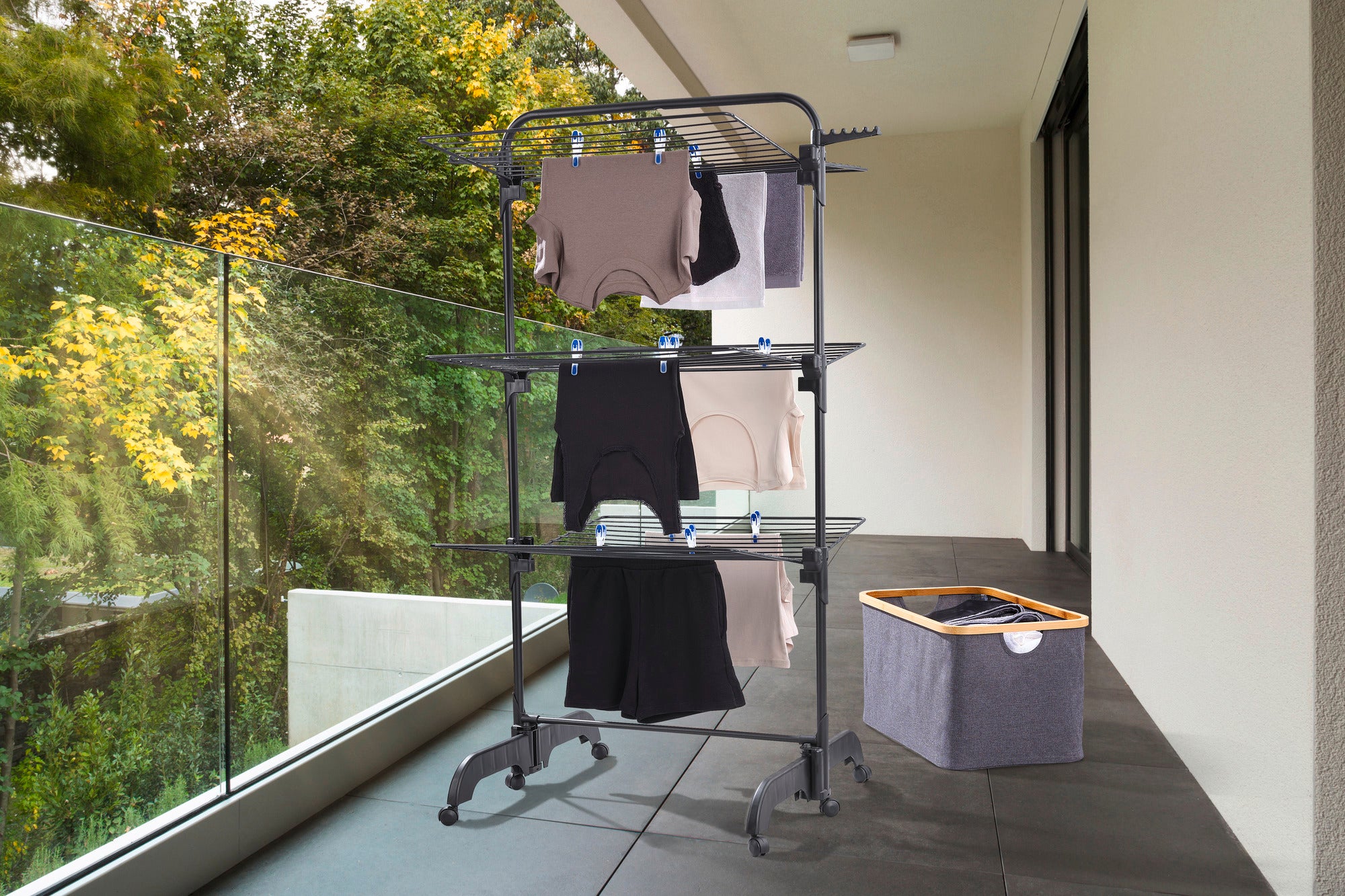 Comfort Tower 420 Black tower dryer on a balcony. The dryer is loaded with several items of clothing and stands next to a laundry basket. Ideal for space-saving drying.