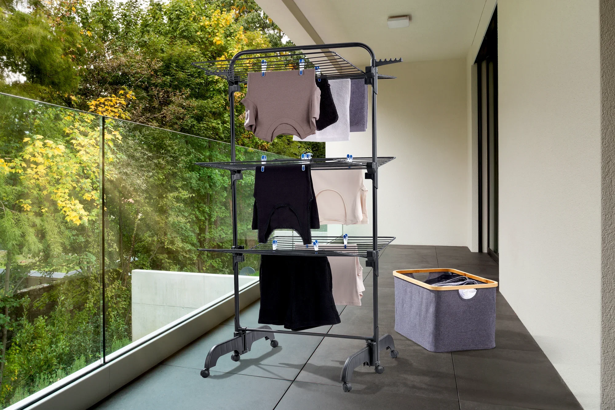 Sèche-linge à tour Comfort Tower 420 Black sur un balcon. Le sèche-linge est chargé de plusieurs vêtements et se trouve à côté d'un panier à linge. Idéal pour un séchage peu encombrant.