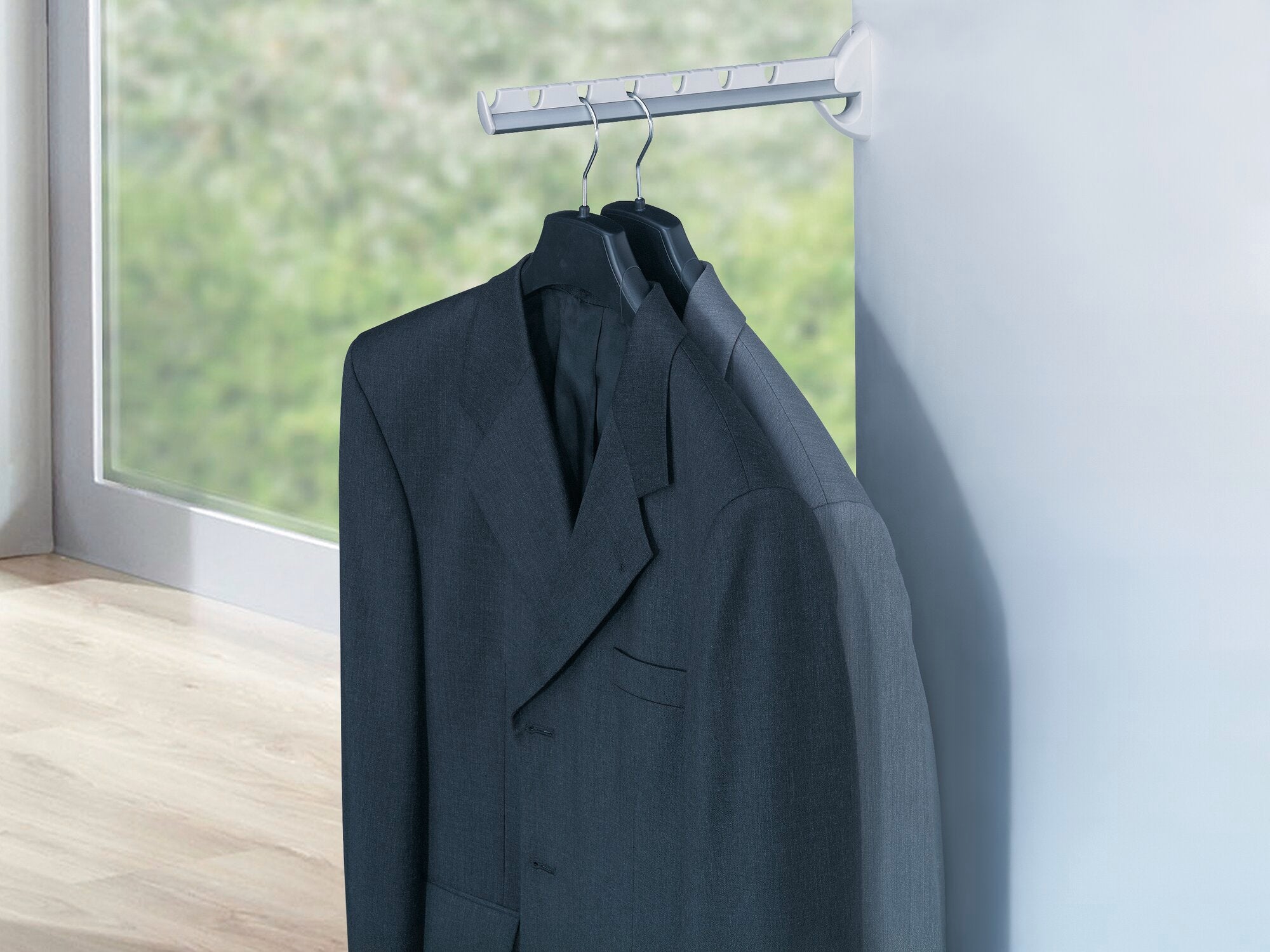 Een Airette wandklerenairer toont meerdere pakken op hangers. De ventilator biedt een ruimtebesparende oplossing voor het opbergen van kleding.