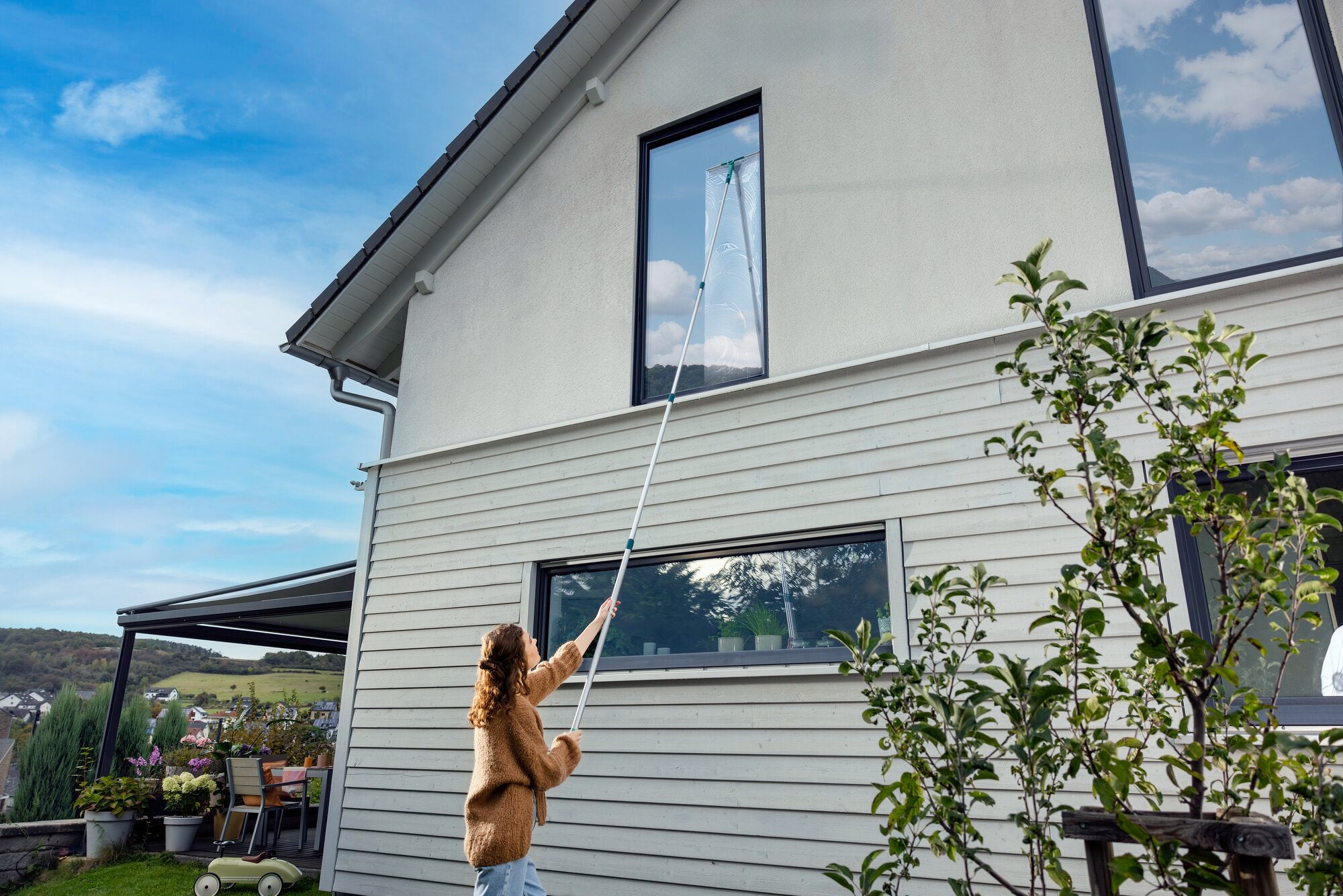 Eine Person verwendet den 2in1 XL ProReach Abzieher, um ein hohes Fenster eines modernen Hauses zu reinigen. Der Abzieher hat einen langen Griff, ideal für schwer erreichbare Stellen.