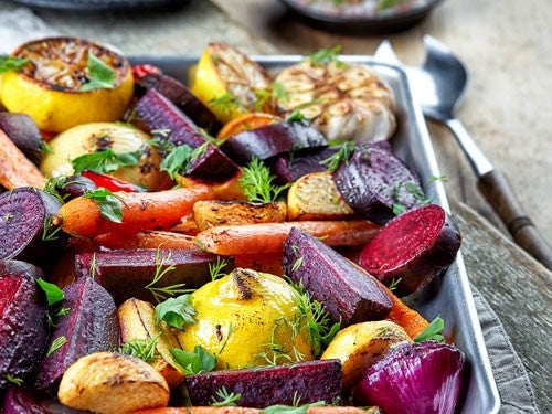 Ein Blech mit geroestetem Ofengemuese wie Karotten, Rote Beete, Zitronen und Knoblauch, garniert mit frischen Kraeutern.