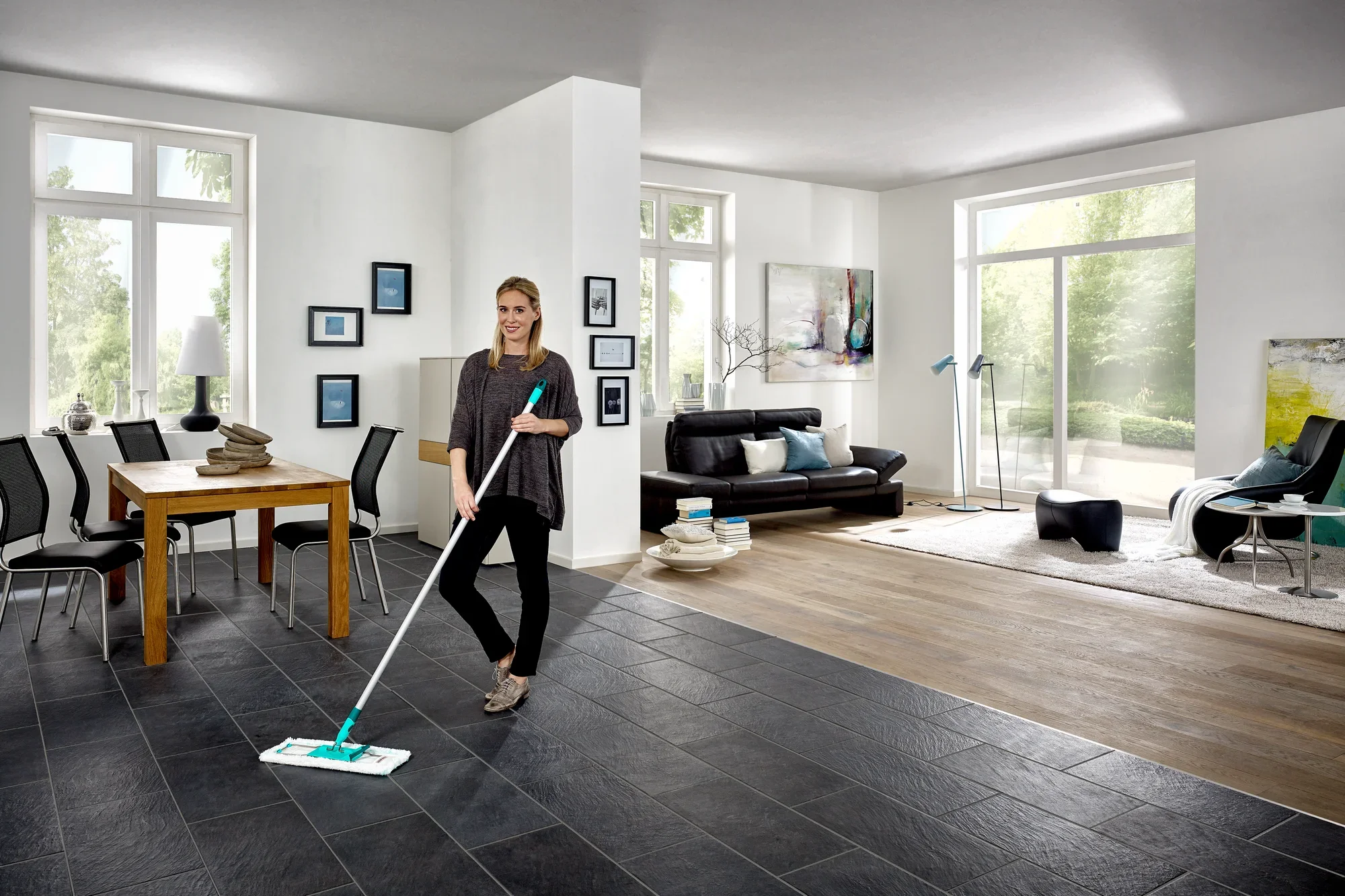 Een vrouw dweilt de vloer van een moderne woonkamer met de Profi XL dweilmop. De kamer is licht en stijlvol ingericht, met grote ramen en elegante meubels.