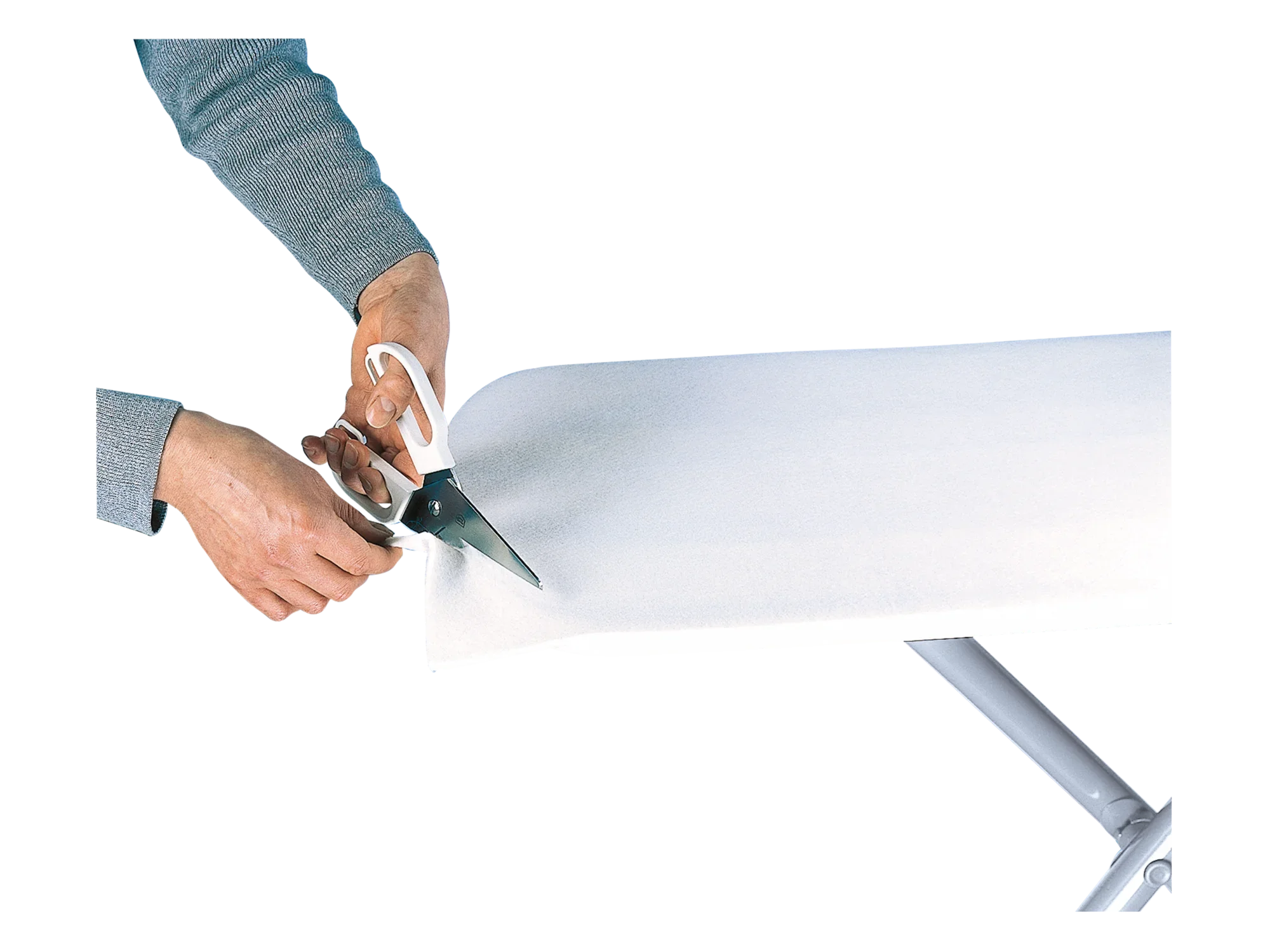 Eén persoon gebruikt een schaar om een witte strijkplankmat op maat te knippen. De onderlegger wordt op een strijkplank bevestigd en zorgvuldig op maat geknipt.