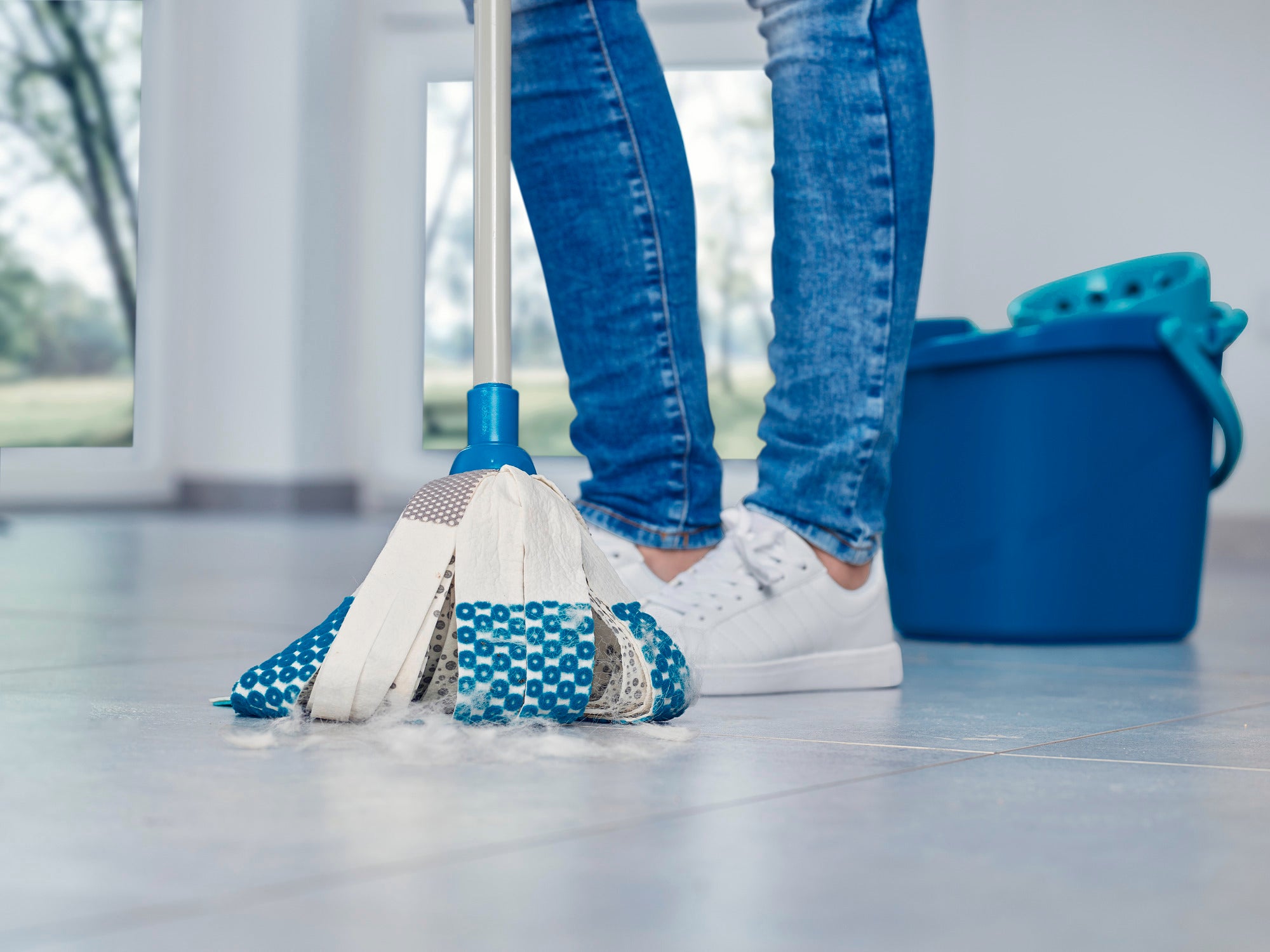 Ein Mensch reinigt einen hellen Boden mit dem Power Mop 3in1. Der Wischmopp hat blaue und weiße Streifen und wird neben einem blauen Eimer verwendet. Ideal für gründliche Reinigung.