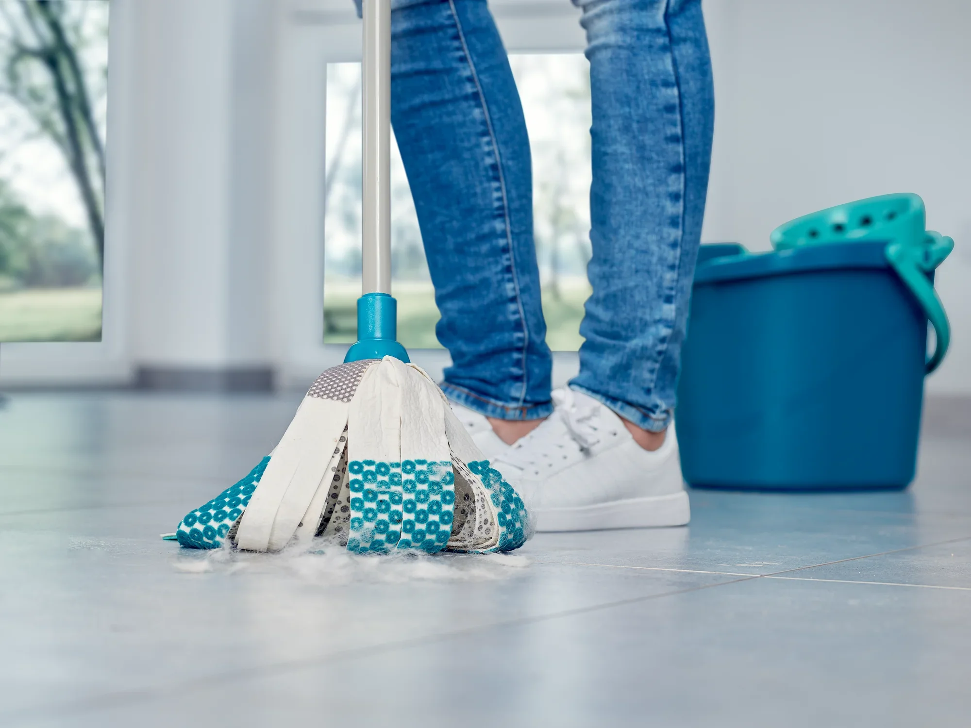 A person is cleaning a light-coloured floor with the Power Mop 3in1. The mop has blue and white stripes and is being used next to a blue bucket. Ideal for thorough cleaning.