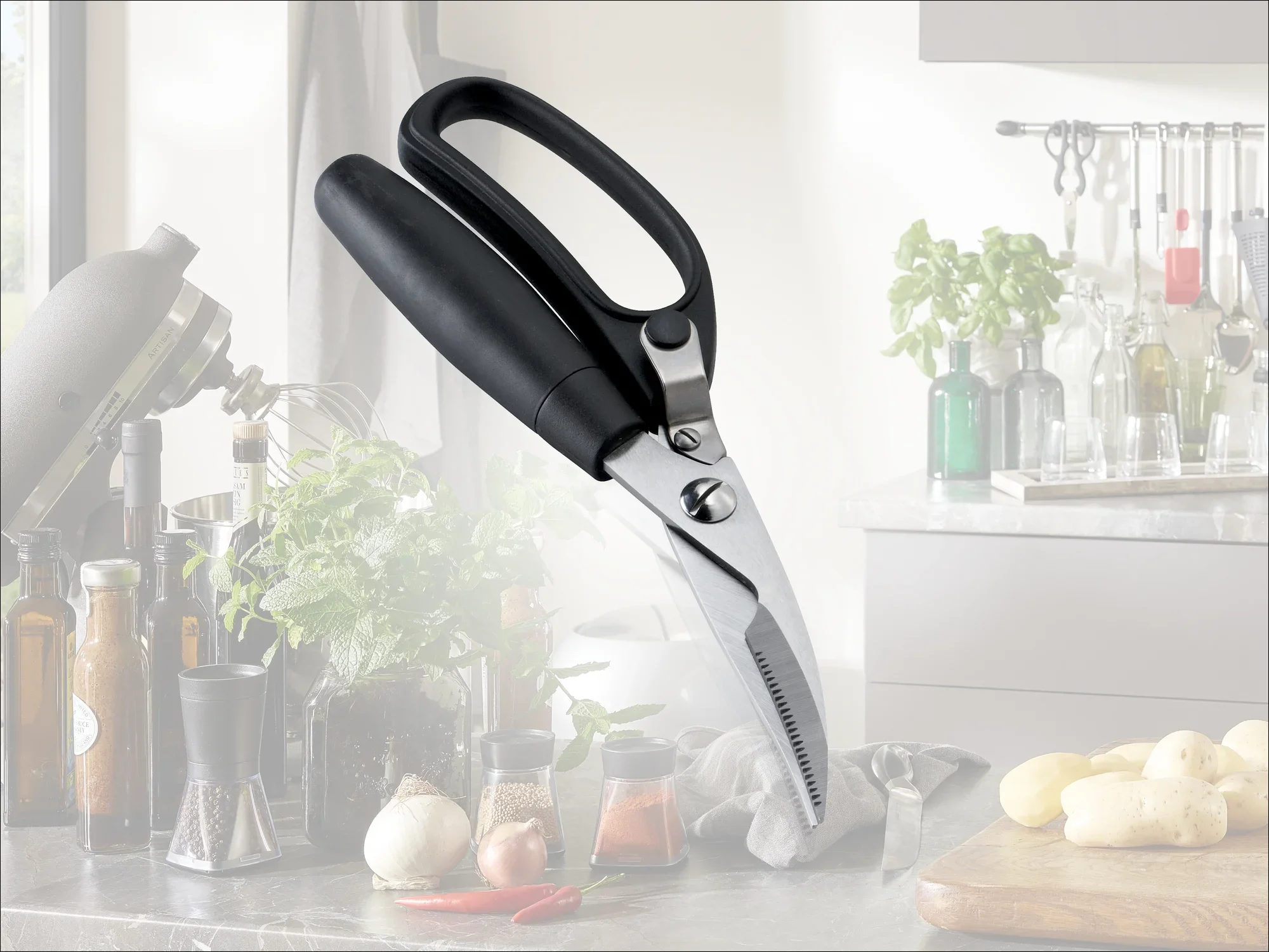 Nożyce kuchenne z czarnym uchwytem na blacie kuchennym. W tle widoczne są przyprawy, zioła i przybory kuchenne. Idealne do wszechstronnego cięcia.