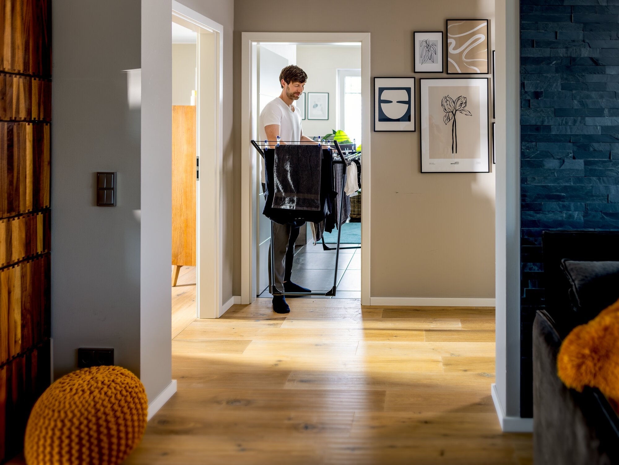 Leifheit Pegasus Slim 15m Black Wäscheständer in Schwarz wird von einem Mann durch den Flur getragen; das schlanke, platzsparende Design eignet sich ideal für kleine Wohnungen und enge Räume.