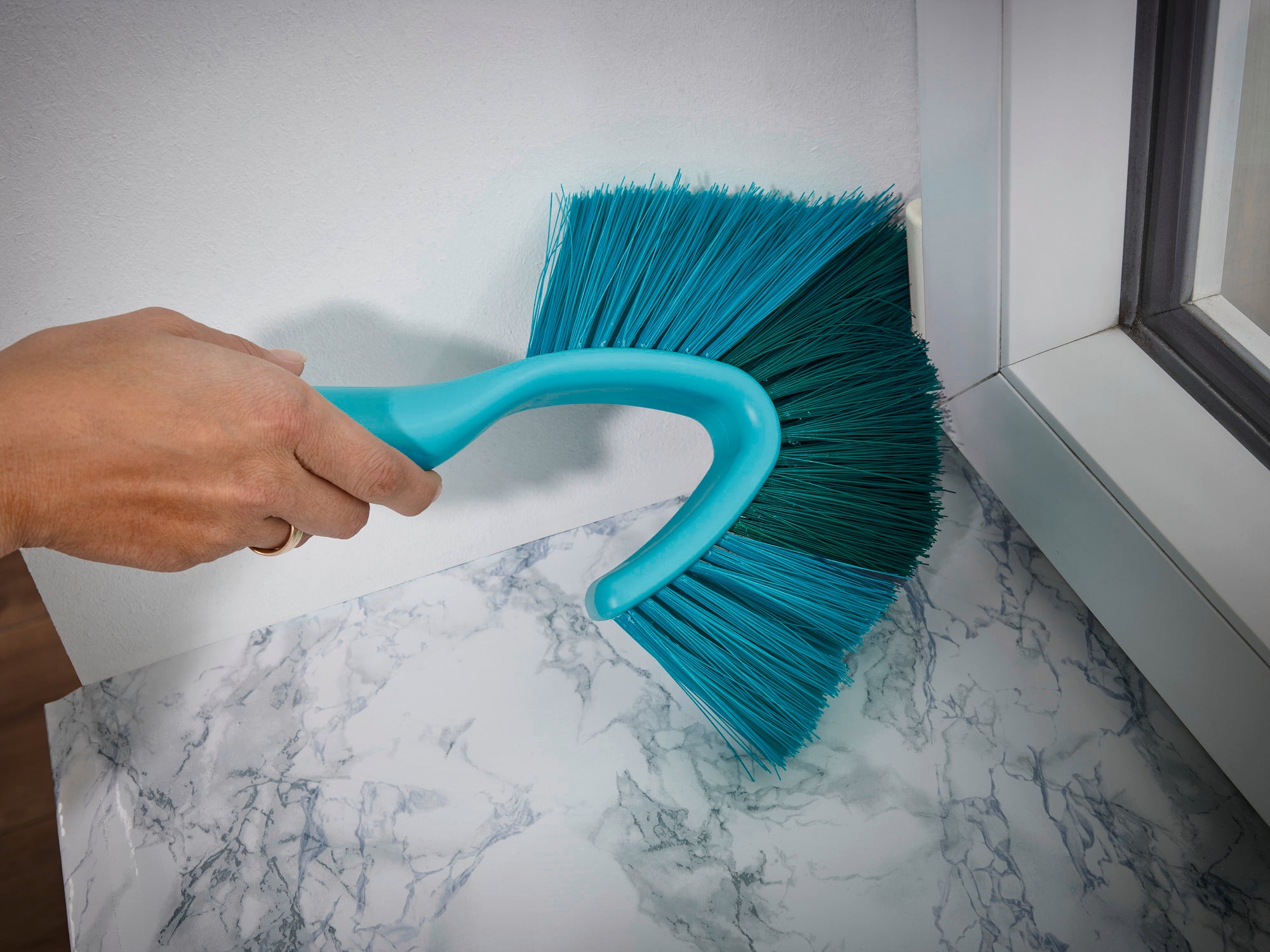 Ein Hand hält den SUPERDUSTER Staubbesen mit Teleskopstiel, um Staub von einer Marmoroberfläche zu entfernen. Der Besen hat blaue Borsten und einen ergonomischen Griff.