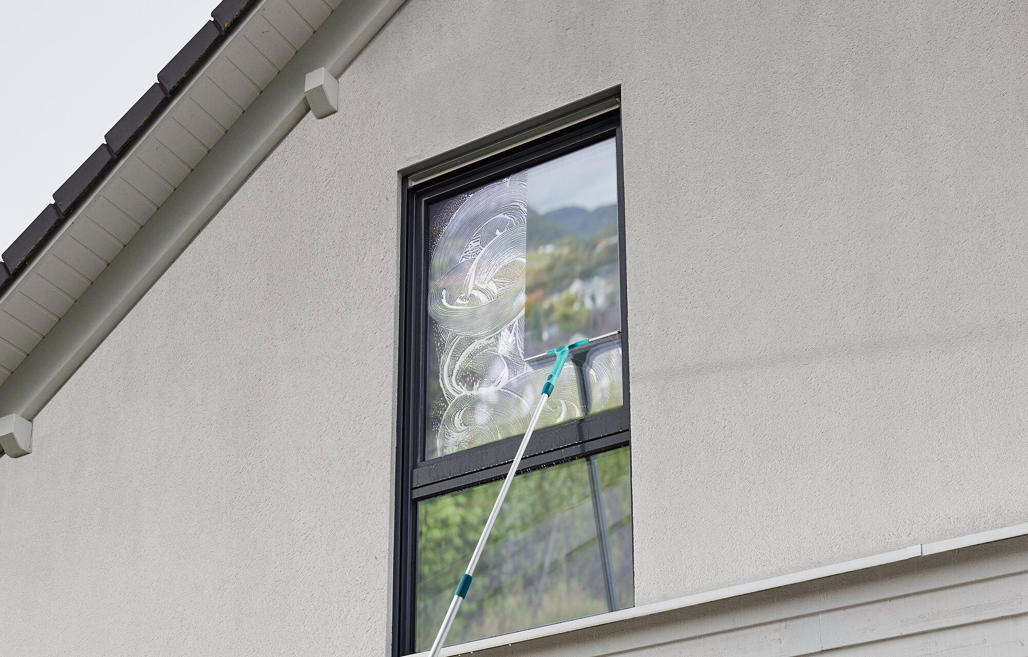 Ein Fensterreiniger verwendet das 2in1 XL ProReach Set, um ein hohes Fenster von außen zu reinigen. Der lange Stiel ermöglicht eine einfache und sichere Reinigung.