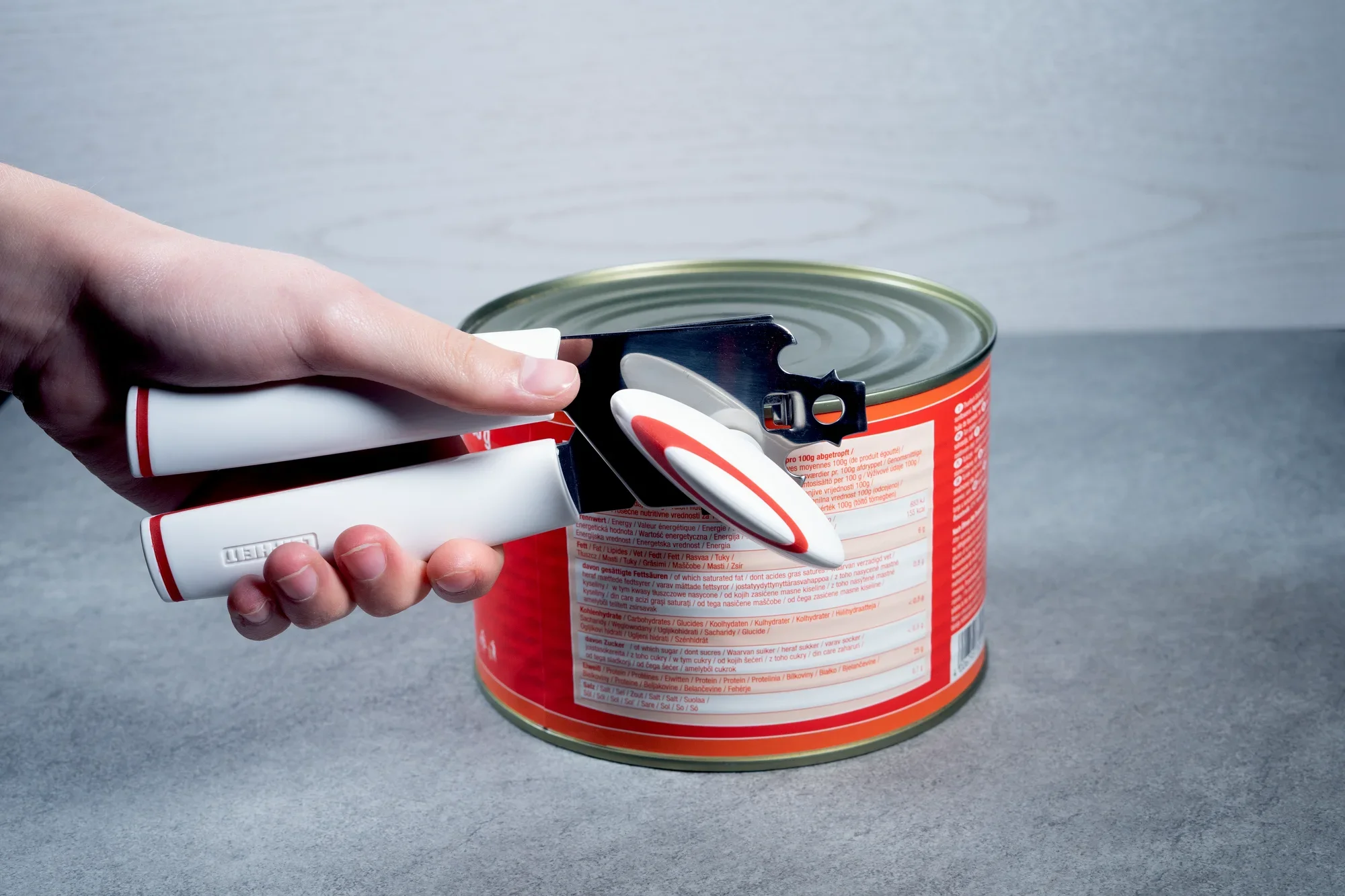 Ein Dosenöffner namens "Lifty" wird verwendet, um eine große Dose zu öffnen. Eine Hand hält den ergonomisch gestalteten Öffner, während die Klinge den Dosenrand schneidet.