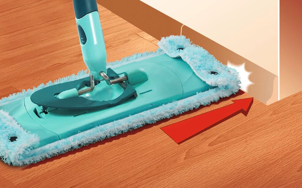 Een turquoise CLEAN TWIST mop maakt de vloer langs een muur grondig schoon. De rode pijl geeft gemakkelijke toegang tot moeilijk bereikbare plaatsen aan.