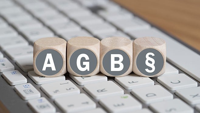 Vier hoelzerne Wuerfel mit den Buchstaben A, G, B und dem Paragraphensymbol stehen auf einer Computertastatur.
