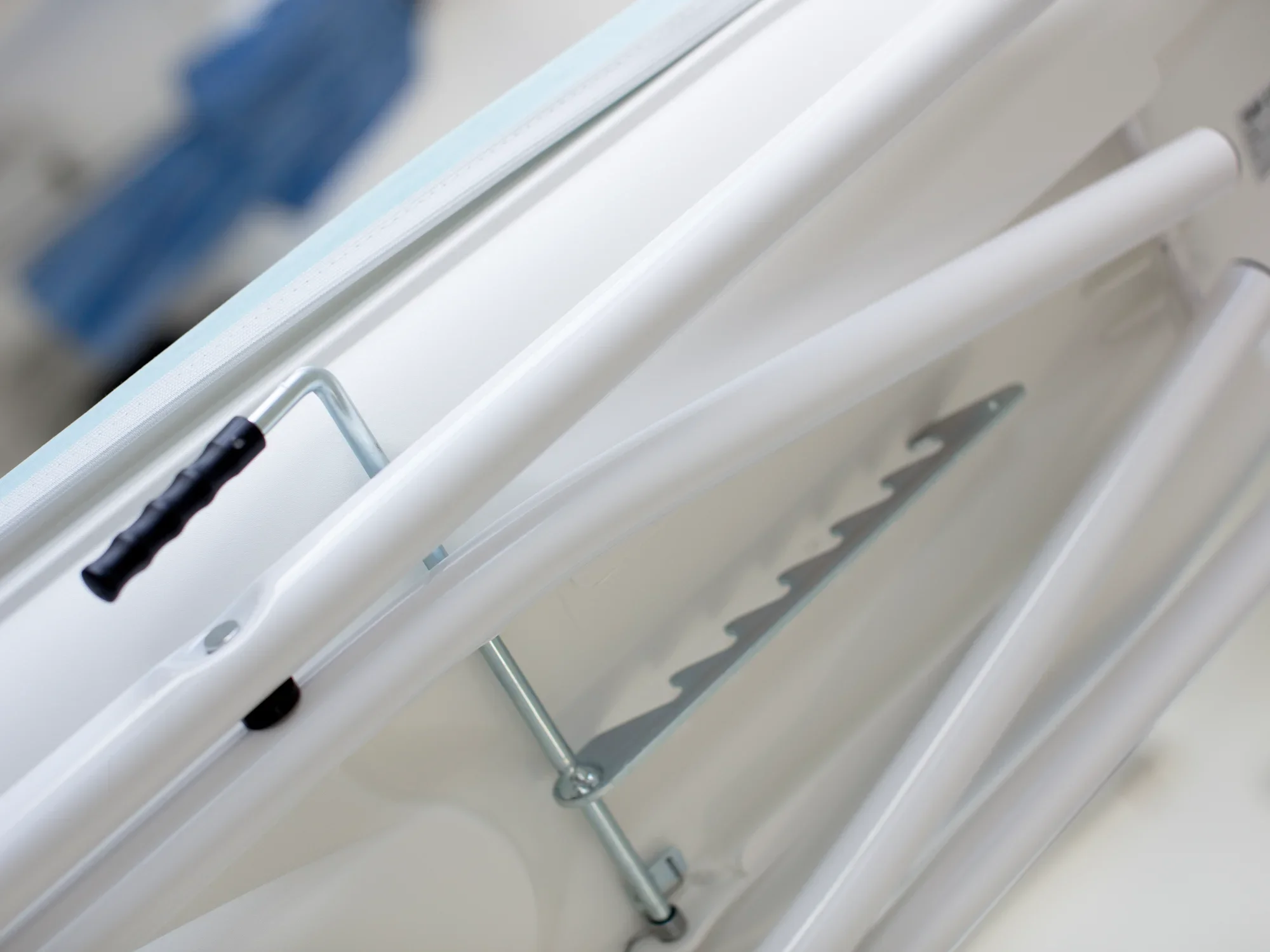 Table à repasser Air Active Express M en blanc, gros plan sur le dessous avec renforts métalliques et poignée. La table offre stabilité et fonctionnalité pour un repassage efficace.