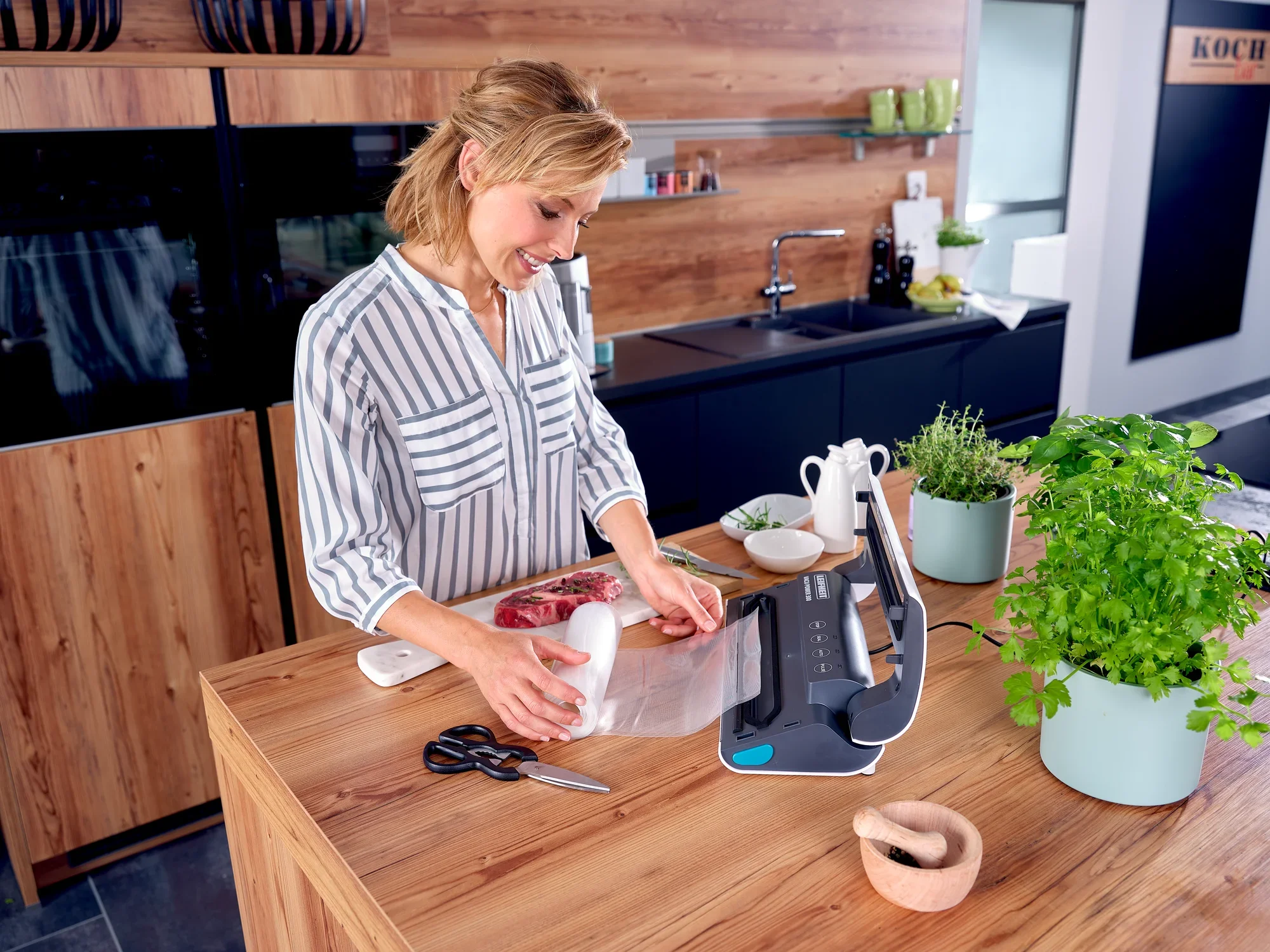 Kobieta używa zgrzewarki próżniowej Vacu Power 300 w nowoczesnej kuchni. Uszczelnia próżniowo mięso, aby zachować jego świeżość. Zioła i przybory kuchenne znajdują się na blacie roboczym.