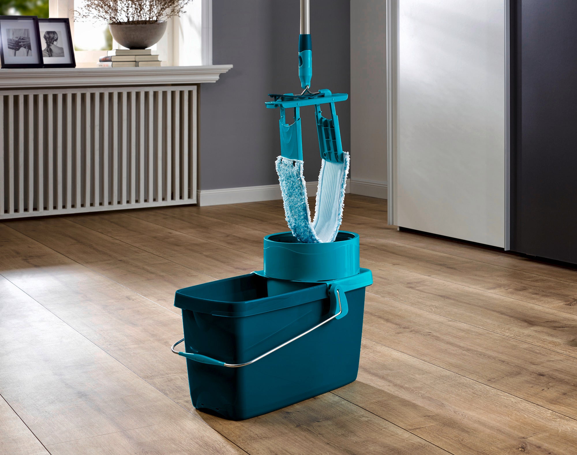 Een CLEAN TWIST System M in een moderne kamer. De emmer is turkoois en voorzien van een draaimechanisme, ideaal voor het efficiënt en moeiteloos reinigen van vloeren.