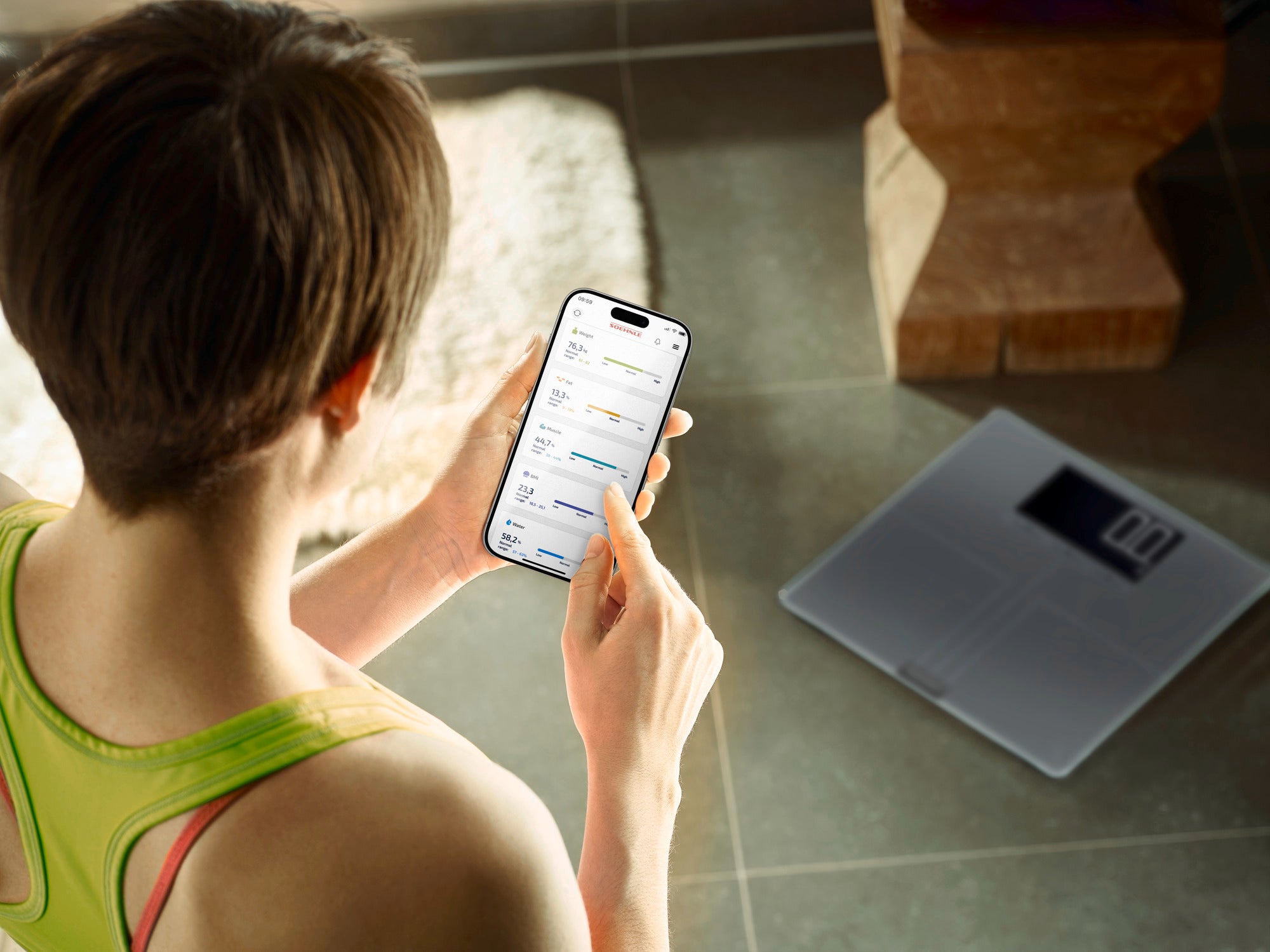 Eine Person nutzt die Personenwaage digital Shape Sense Connect 200. Sie hält ein Smartphone, das die Verbindung zur Waage zeigt, um Gesundheitsdaten zu überwachen.