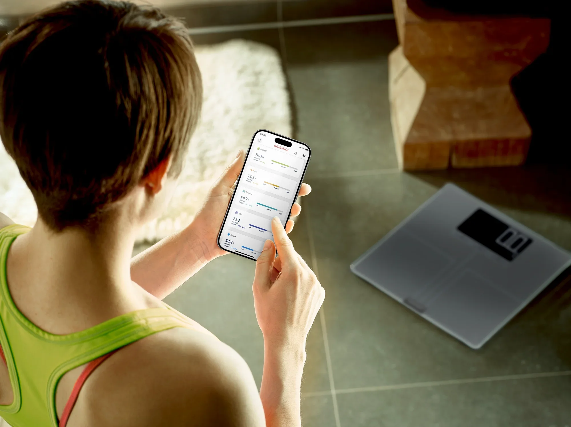 Osoba korzysta z cyfrowej wagi łazienkowej Shape Sense Connect 200, trzymając smartfon, który pokazuje połączenie z wagą w celu monitorowania danych zdrowotnych.