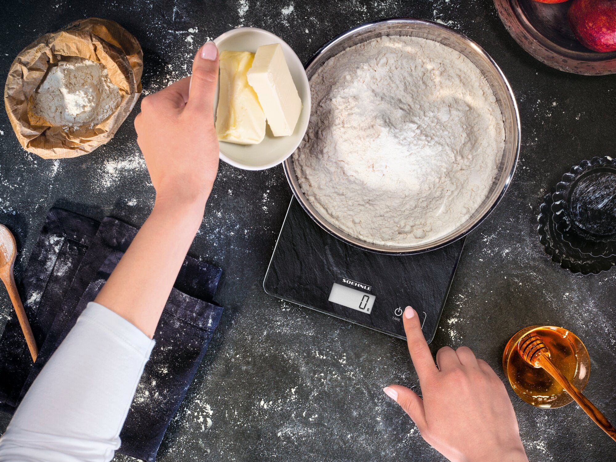 A person weighs flour and butter on the Page Compact 300 Slate digital kitchen scale. The scale displays precise measurements and is ideal for baking recipes.