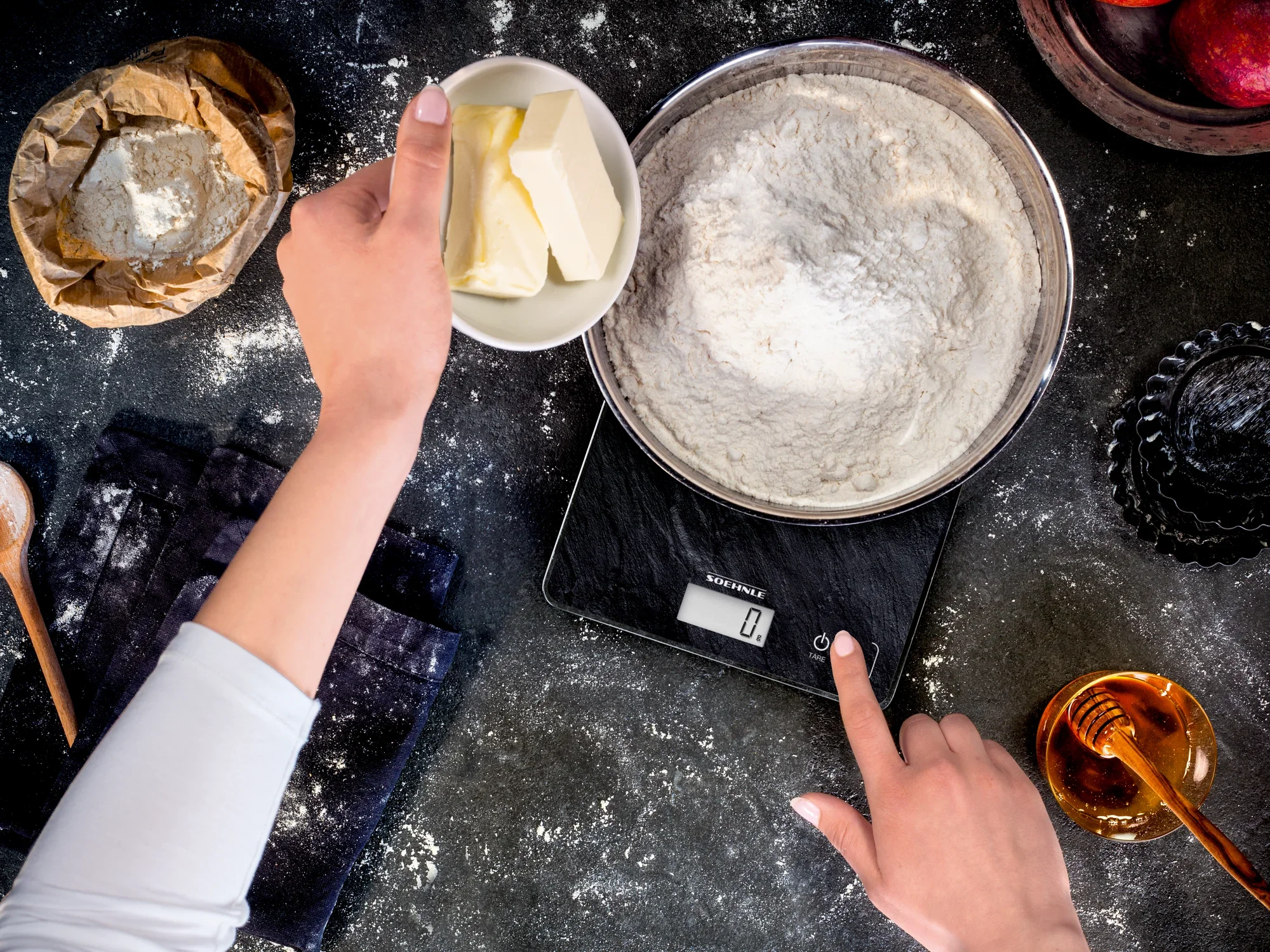 Eine Person wiegt Mehl und Butter auf der digitalen Küchenwaage Page Compact 300 Slate. Die Waage zeigt präzise Messungen an und ist ideal für Backrezepte.
