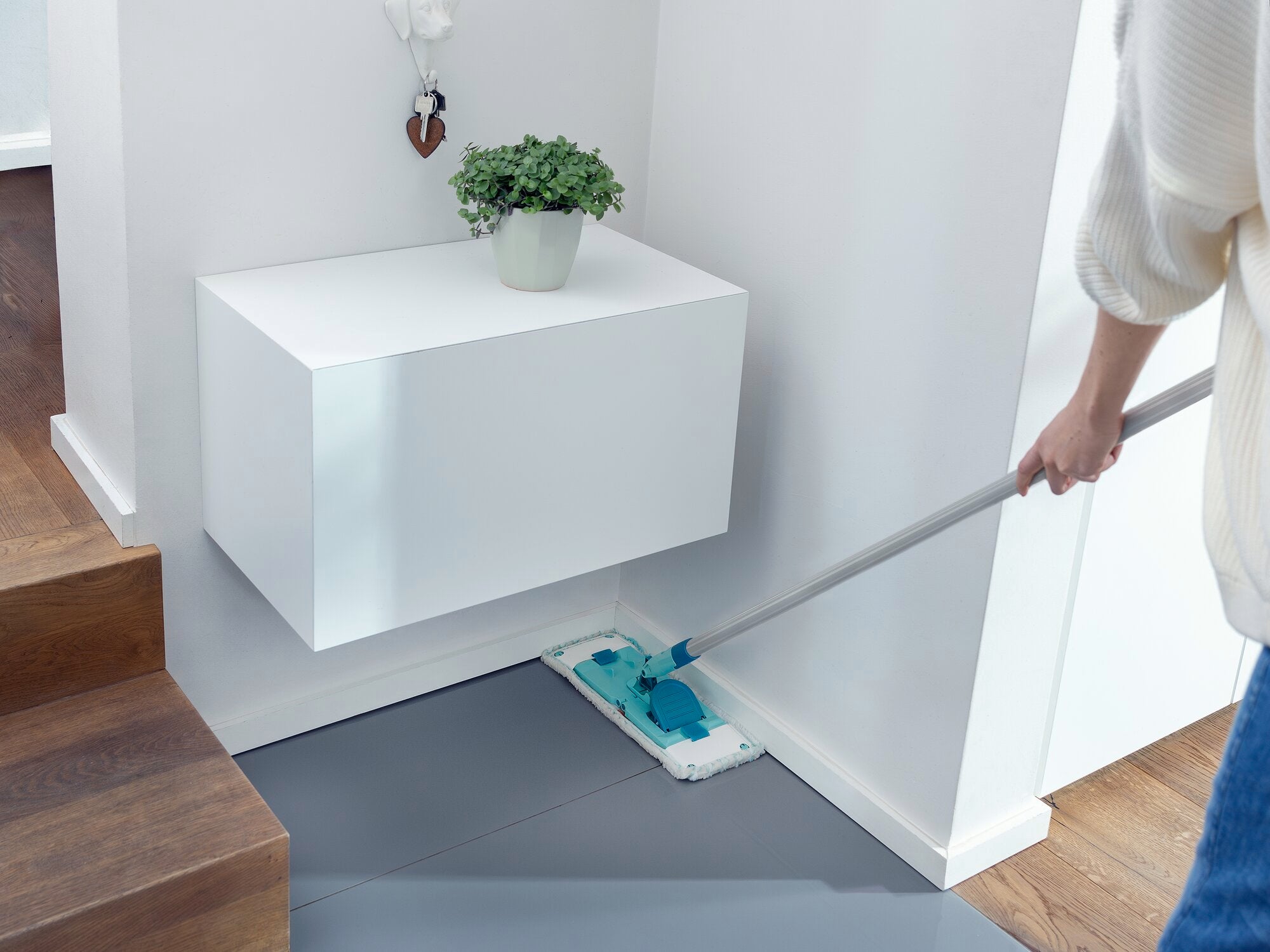 Een persoon dweilt de vloer met de POWER CLEAN M micro duo dweilmop. De mop heeft een blauwe en witte schoonmaakpad en wordt gebruikt in een moderne, lichte omgeving. Ideaal voor een grondige schoonmaakbeurt.