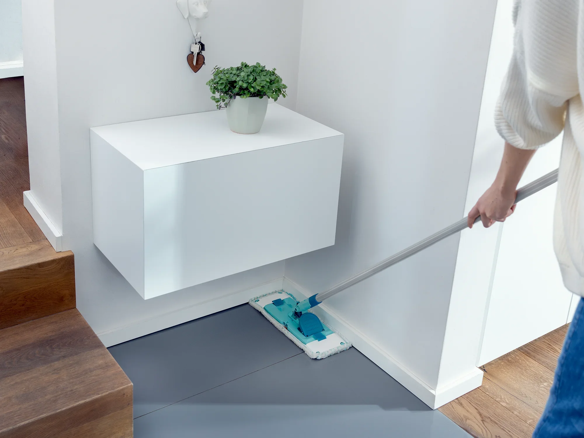 Eine Person reinigt den Boden mit dem Bodenwischer POWER CLEAN M micro duo. Der Wischer hat ein blau-weißes Reinigungspad und wird in einer modernen, hellen Umgebung verwendet. Ideal für gründliche Sauberkeit.