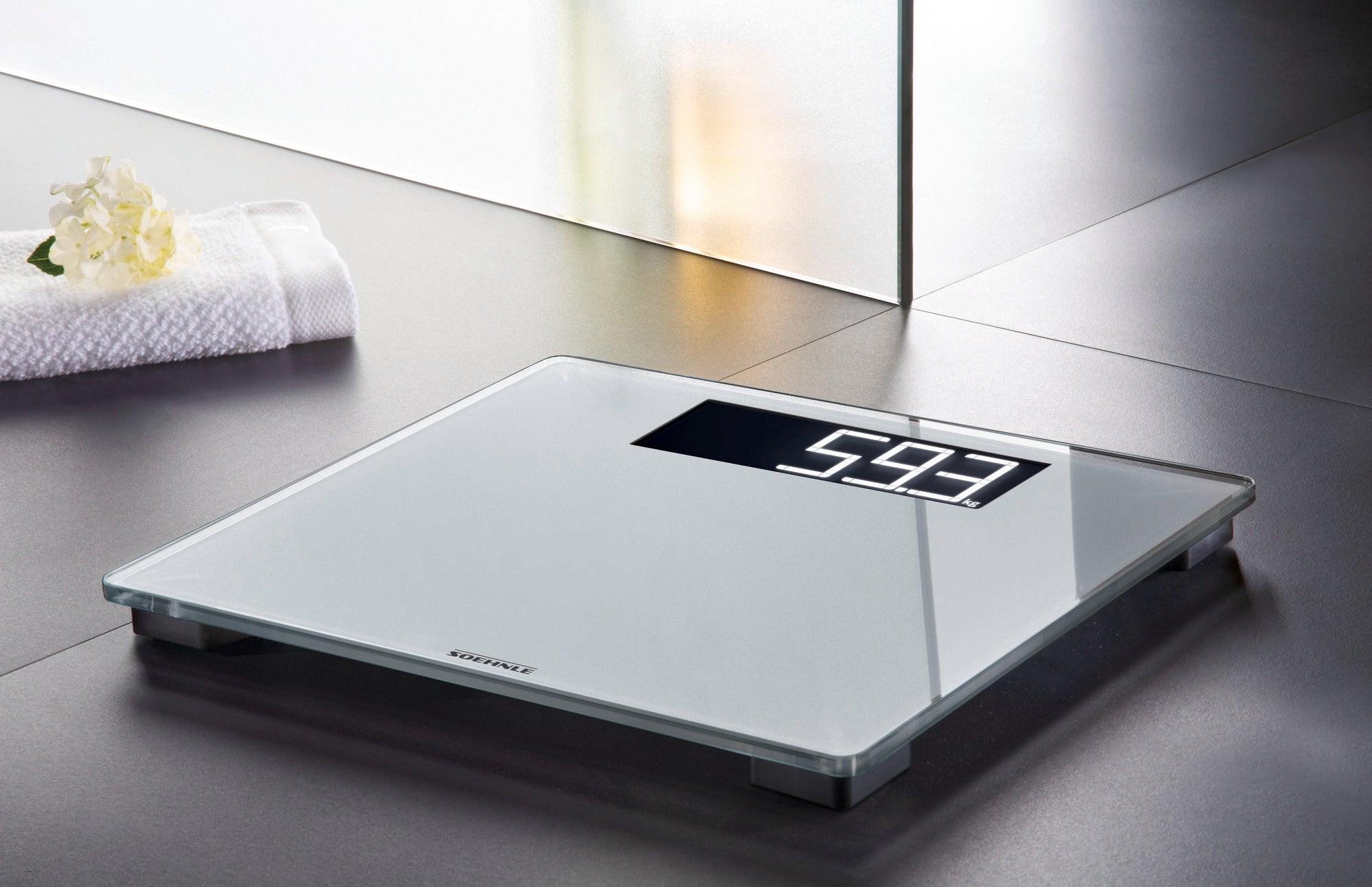 A Style Sense Comfort 600 digital bathroom scale on a modern bathroom floor. The scale shows a weight of 59.3 kg and has an elegant, minimalist design.