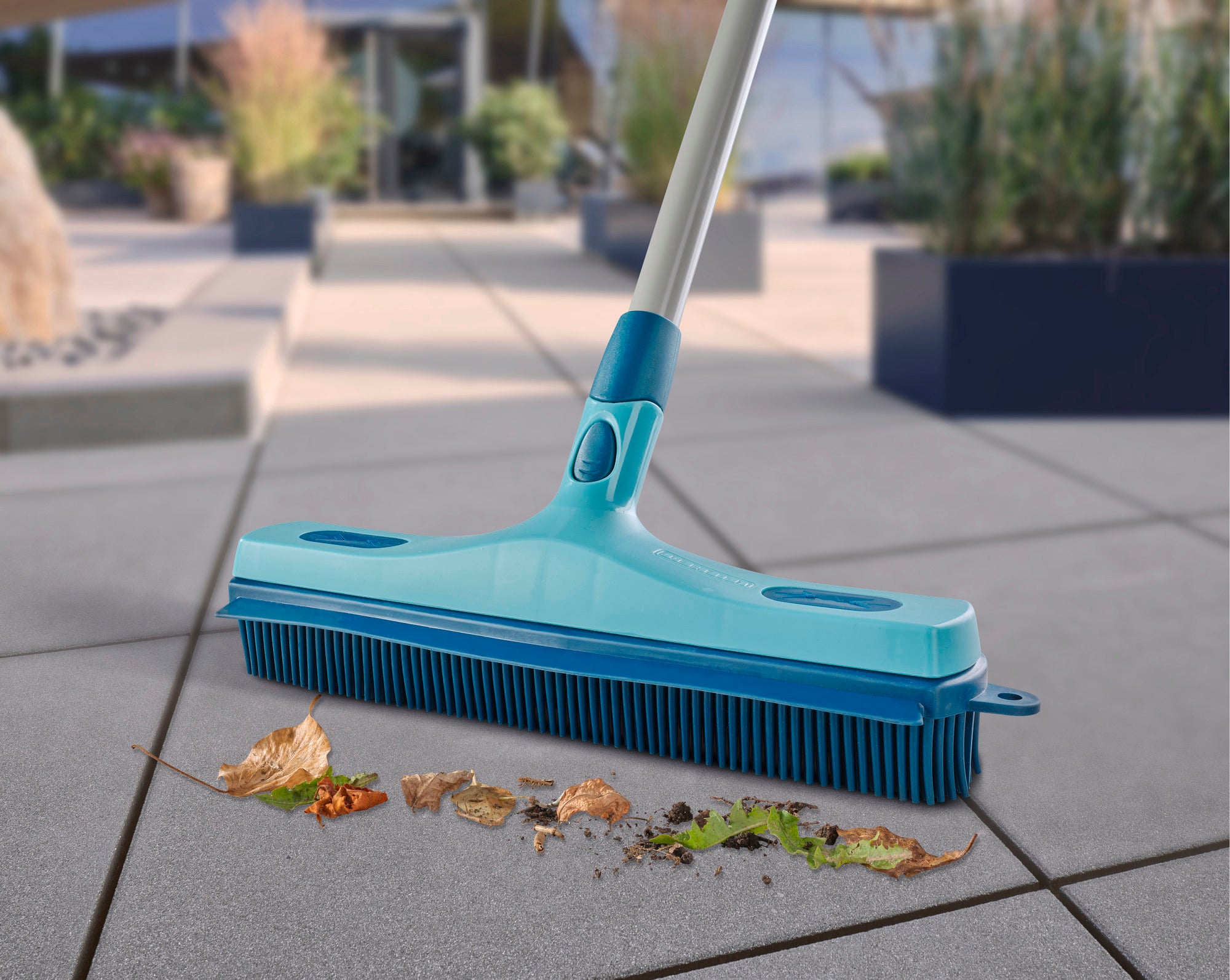 Ein türkisfarbener Gummibesen entfernt effektiv Blätter und Schmutz von einer Terrasse. Ideal für den Außenbereich, um Sauberkeit und Ordnung zu gewährleisten.