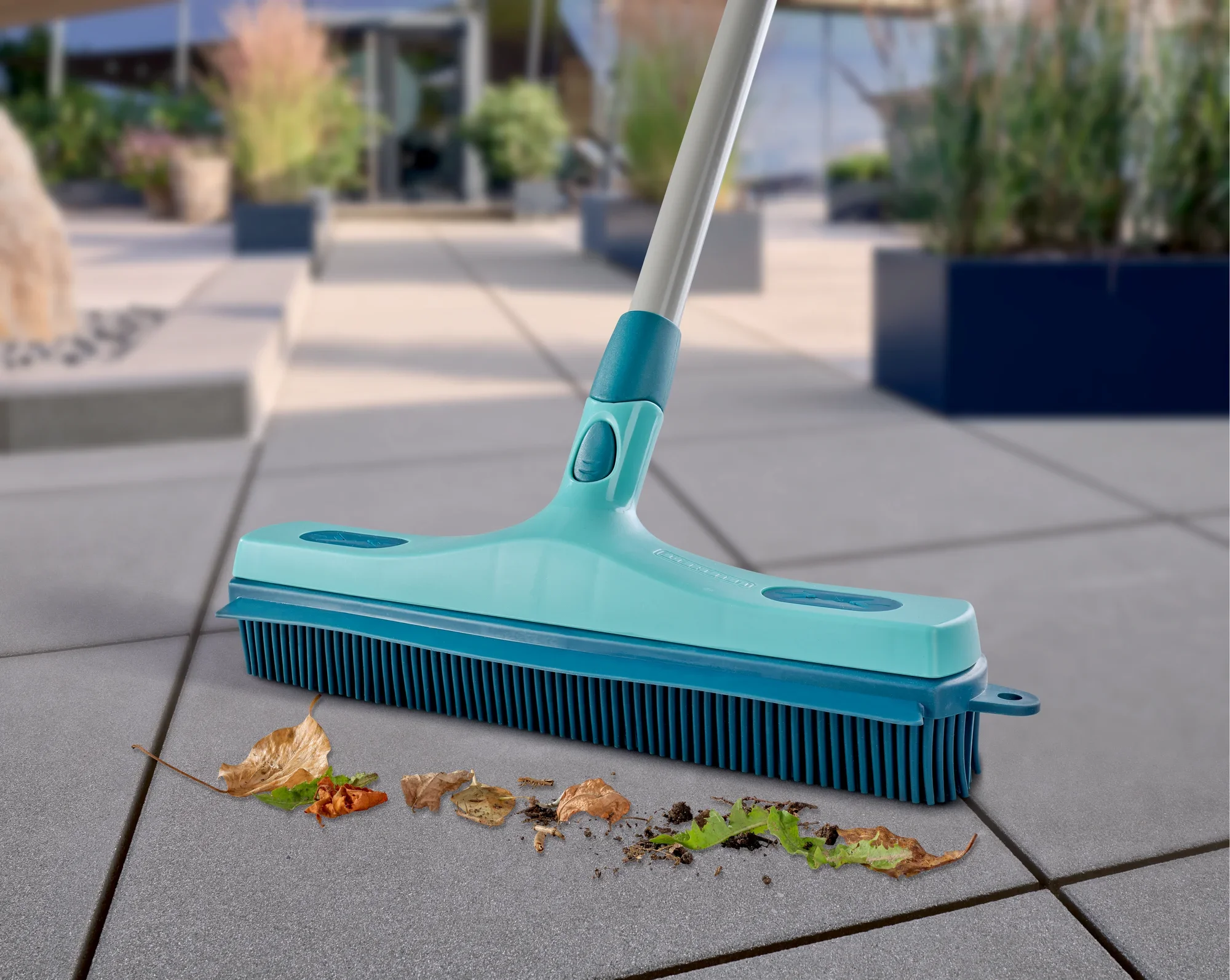 Een turquoise rubberen bezem verwijdert effectief bladeren en vuil van een terras. Ideaal voor buiten om schoon en netjes te blijven.