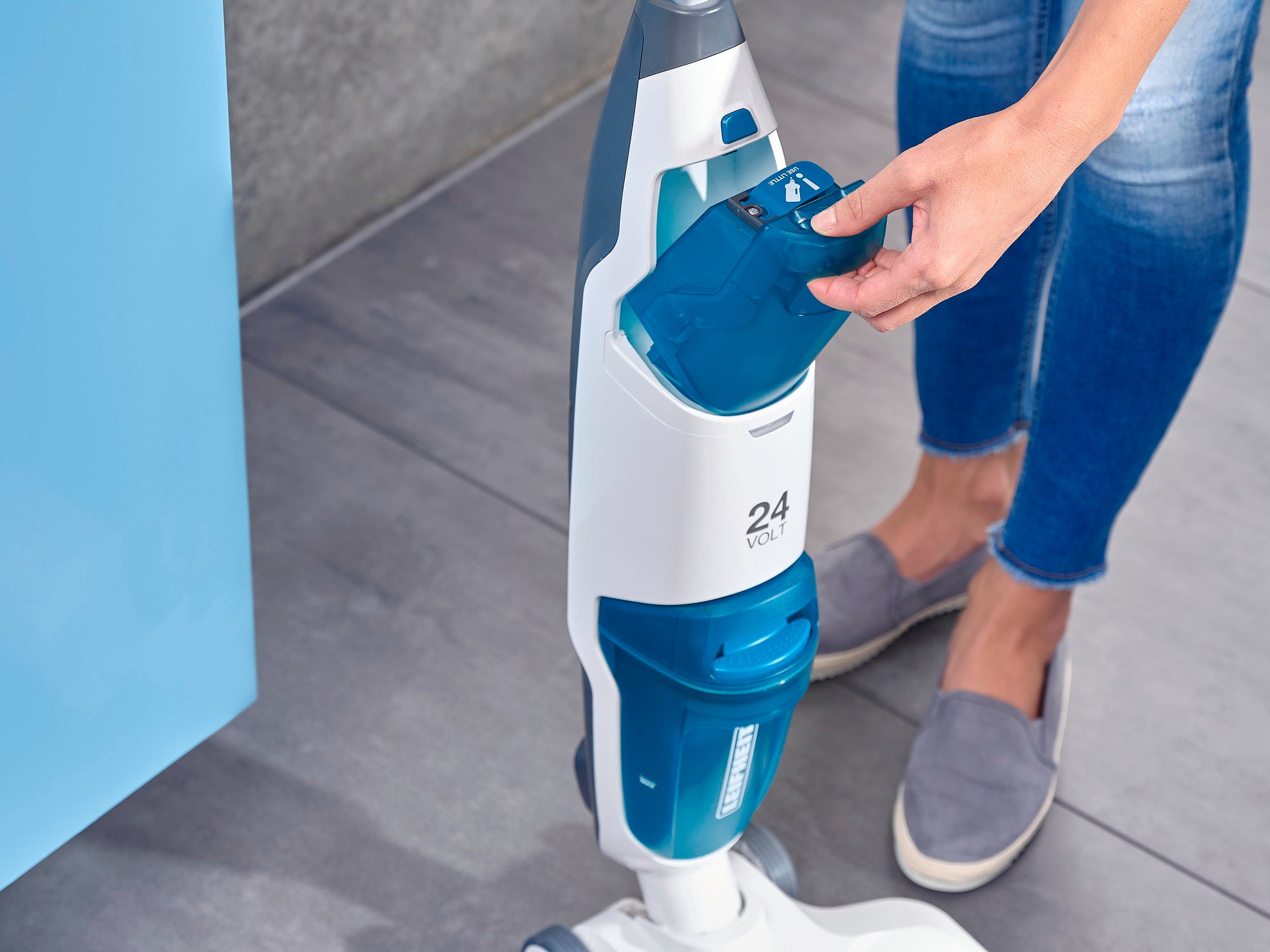 Eine Person bedient den Regulus Aqua PowerVac, einen modernen, blauen und weißen Staubsauger. Der Fokus liegt auf dem Entnehmen des Wasserbehälters. Ideal für effiziente Reinigung.