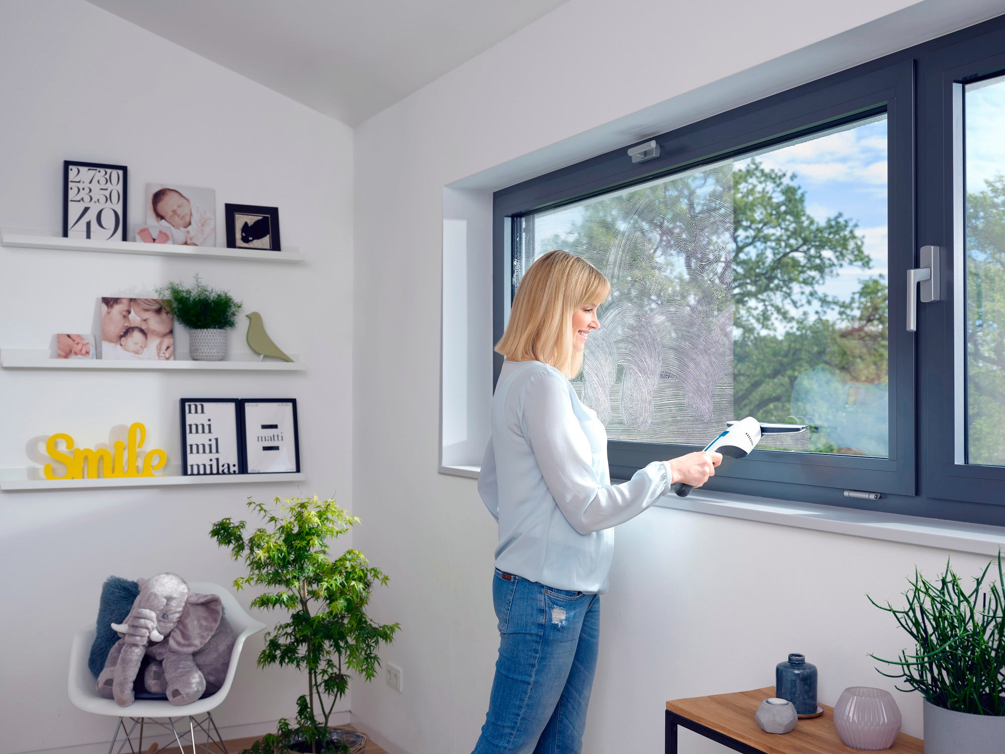 Eine Frau benutzt den Nemo Fenstersauger, um ein großes Fenster zu reinigen. Der Raum ist hell und modern eingerichtet, mit Pflanzen und dekorativen Elementen.