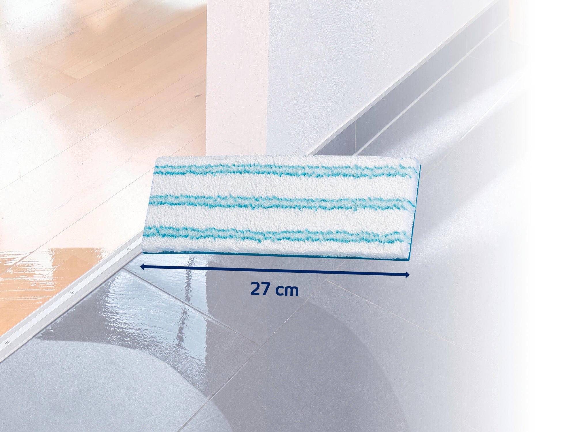 Une tête de balai à franges rectangulaire à rayures bleues repose sur un sol brillant et propre. La tête mesure 27 cm de large et est idéale pour nettoyer en profondeur les sols durs.