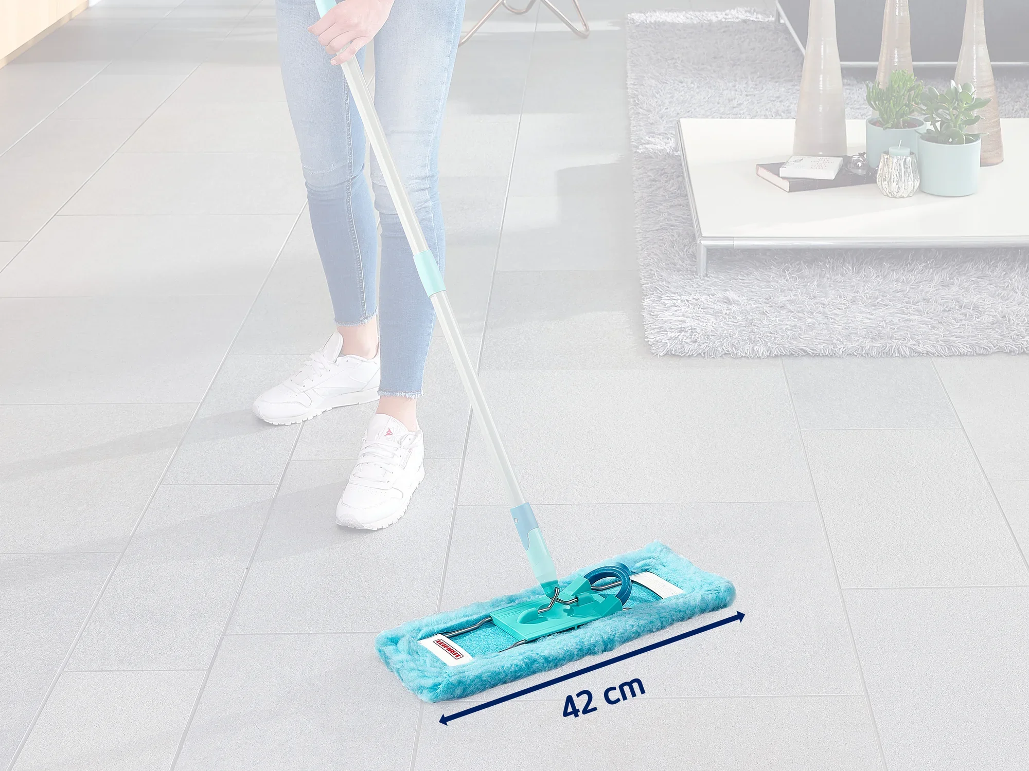 Une personne nettoie un sol carrelé gris avec une serpillière bleue Leifheit 55118. La serpillière a une largeur de 42 cm et est idéale pour les grandes surfaces.
