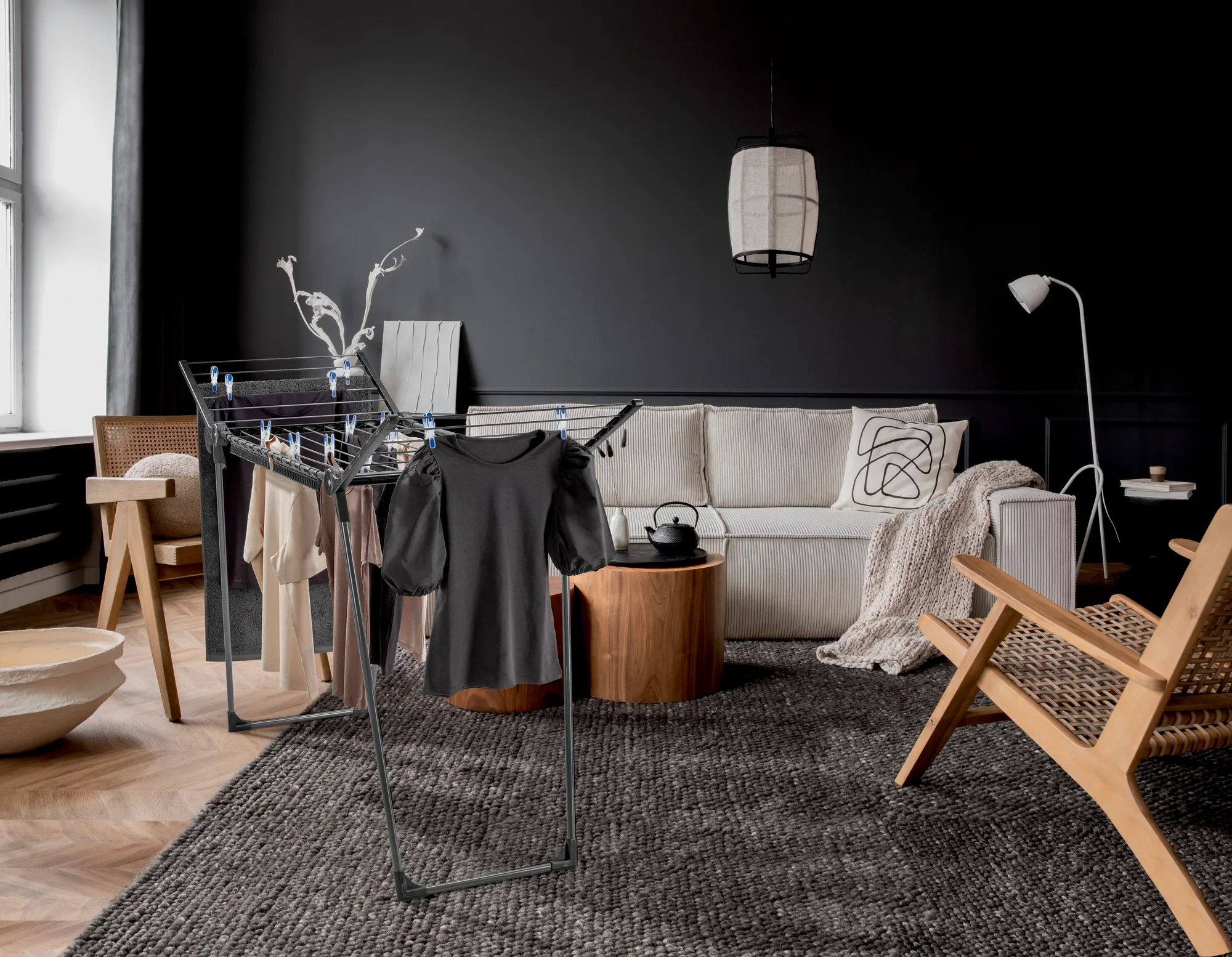 Suszarka bębnowa Pegasus 150 Solid Slim Black w stylowym salonie. Suszarka jest załadowana ubraniami i stoi na nowoczesnym dywanie otoczonym eleganckimi meblami.