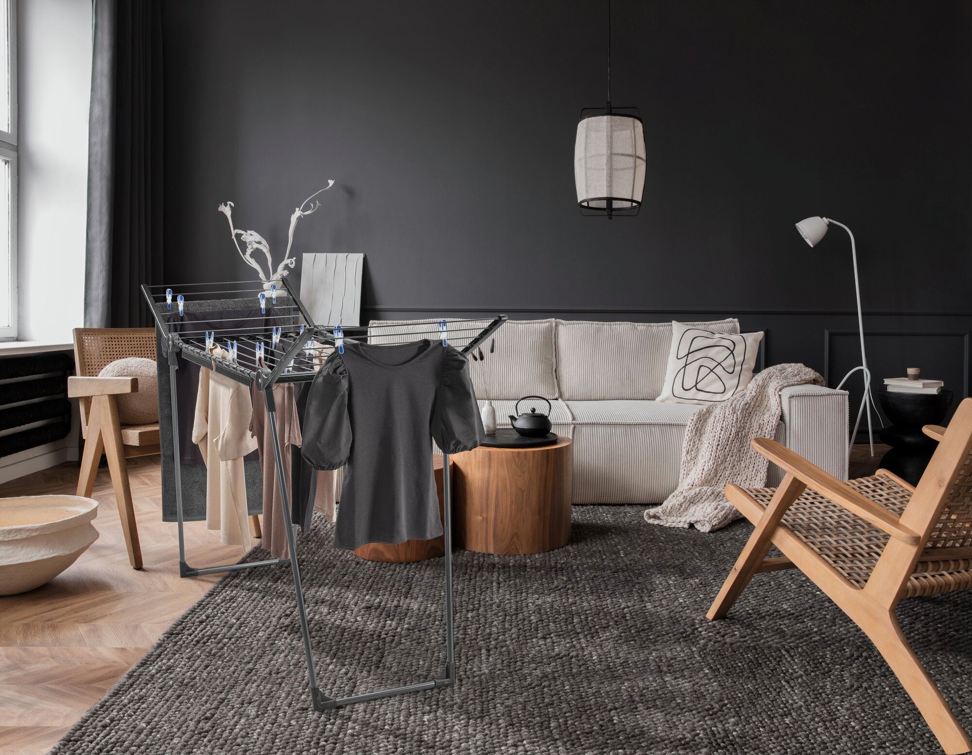 Suszarka bębnowa Pegasus 150 Solid Slim Black w stylowym salonie. Suszarka jest załadowana ubraniami i stoi na nowoczesnym dywanie otoczonym eleganckimi meblami.