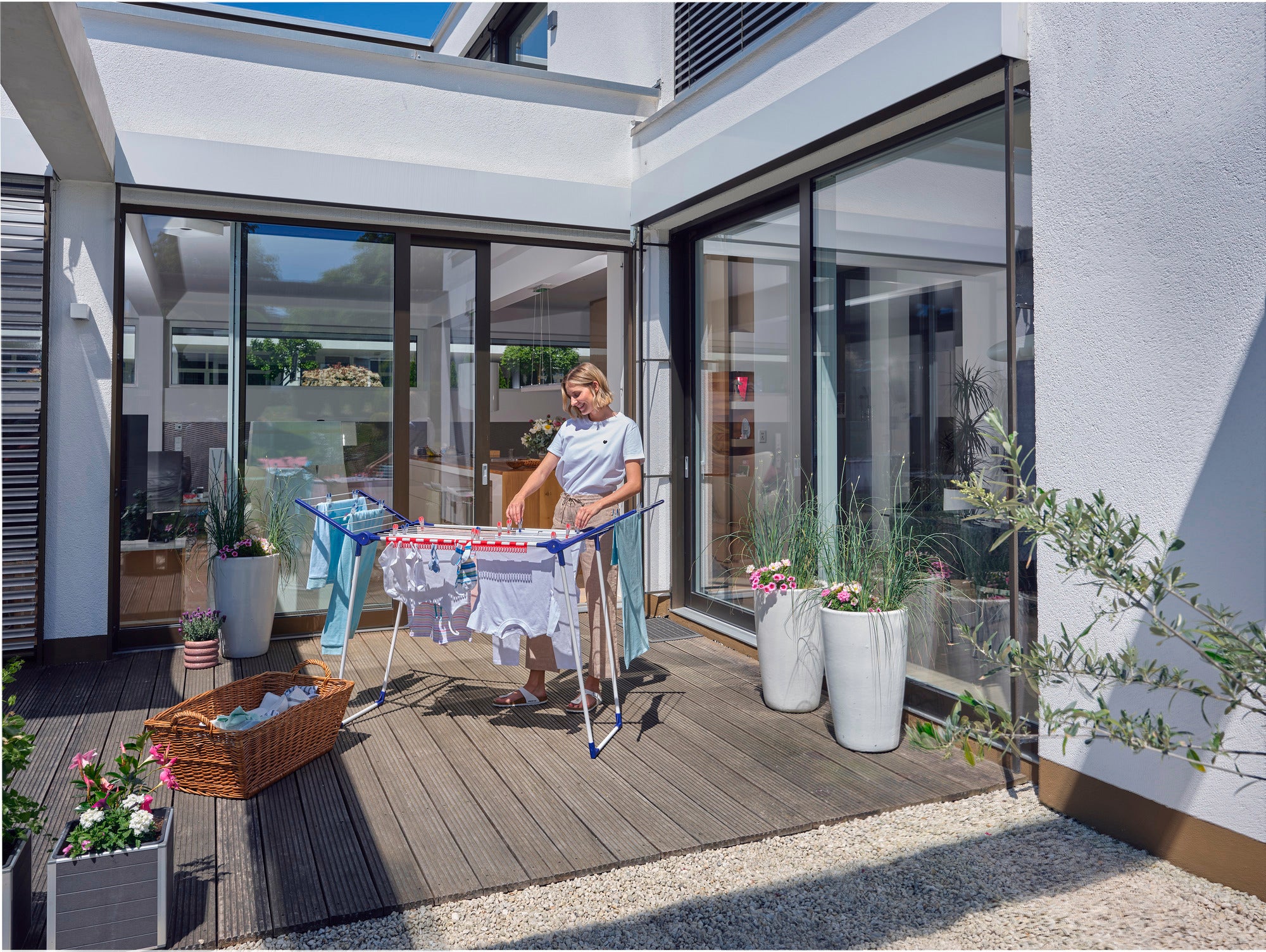 Eine Person steht auf einer Terrasse und benutzt den Standtrockner Pegasus 150 Solid Slim, um frisch gewaschene Kleidung zu trocknen. Der Trockner ist kompakt und ideal für kleine Räume.