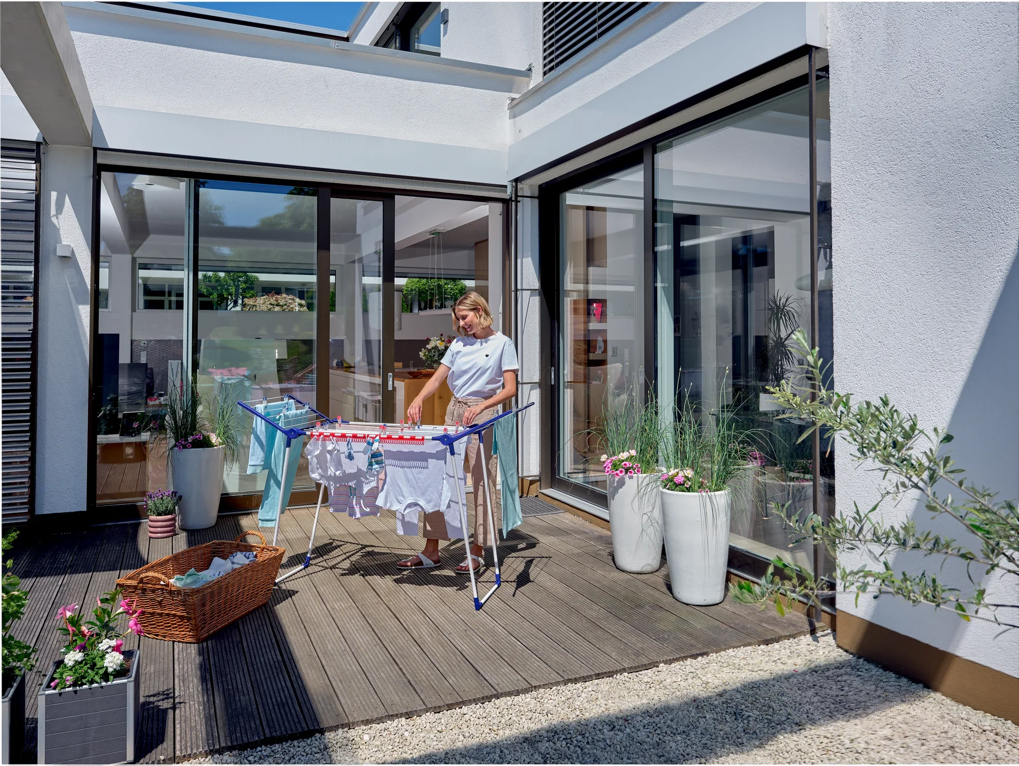 Eine Person steht auf einer Terrasse und benutzt den Standtrockner Pegasus 150 Solid Slim, um frisch gewaschene Kleidung zu trocknen. Der Trockner ist kompakt und ideal für kleine Räume.