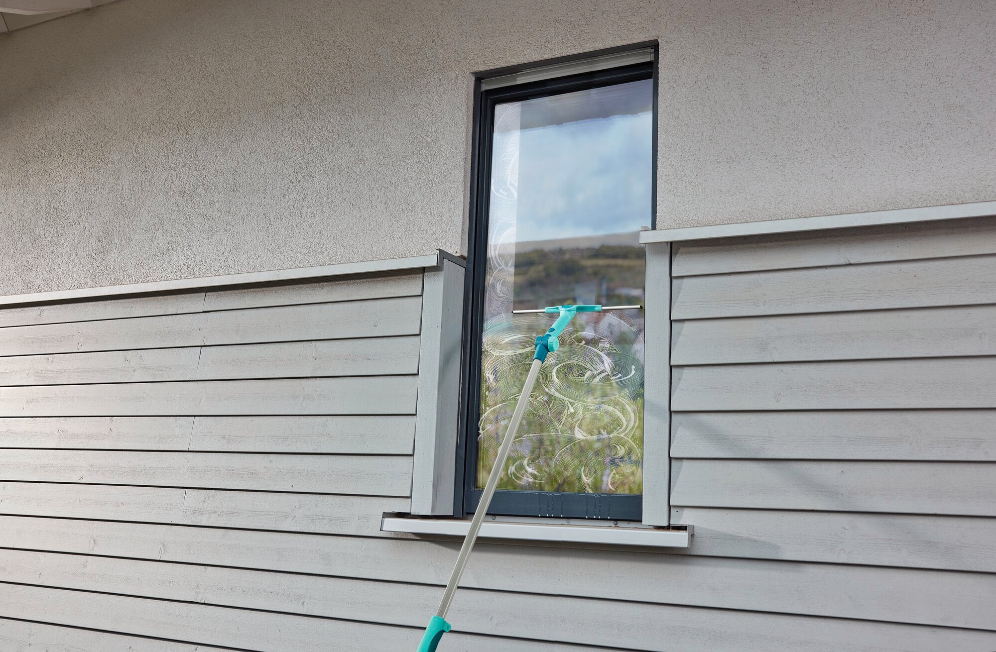 Ein Fensterputzer verwendet den WindowSlider 2in1 XL ProReach Teleskop, um ein hohes Fenster zu reinigen. Der Teleskopstab ermöglicht das Erreichen schwer zugänglicher Stellen.