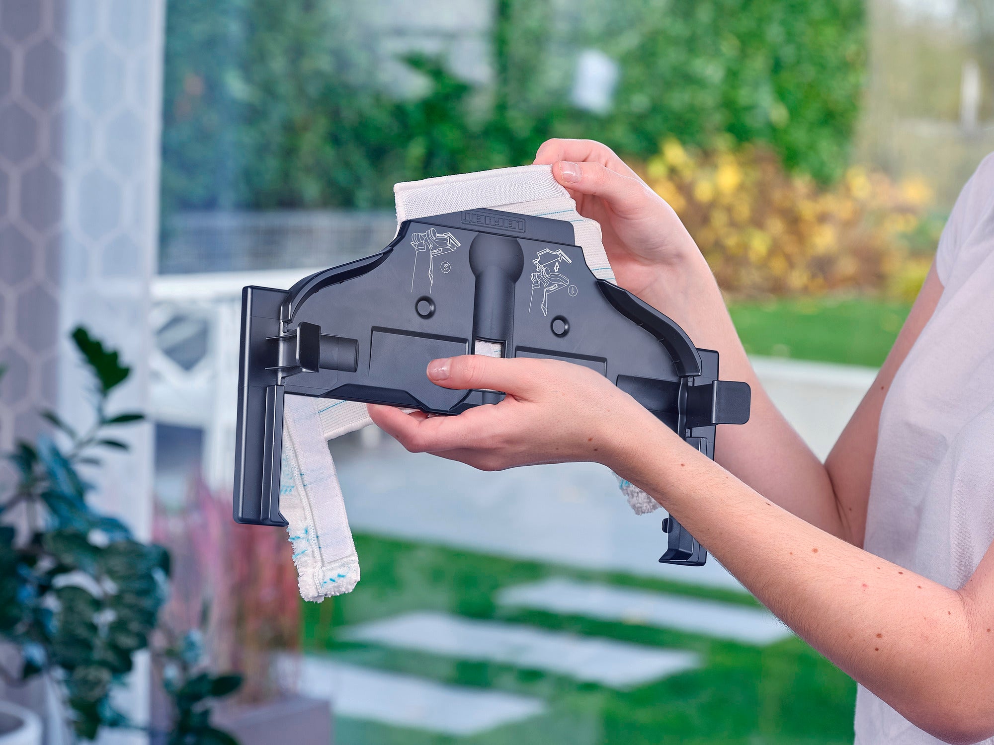 Een persoon houdt de Regulus Aqua PowerVac Pro vast, een geavanceerde stofzuigerkop. De achtergrond toont een groene tuin, wat een frisse en moderne sfeer creëert.