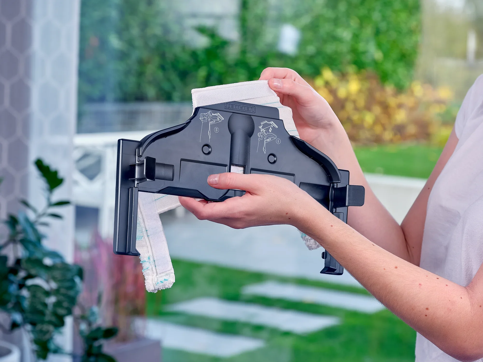 Osoba trzymająca odkurzacz Regulus Aqua PowerVac Pro w jasnym pomieszczeniu z widokiem na ogród. Urządzenie jest pokazane z bliska, co podkreśla jego szczegóły konstrukcyjne.