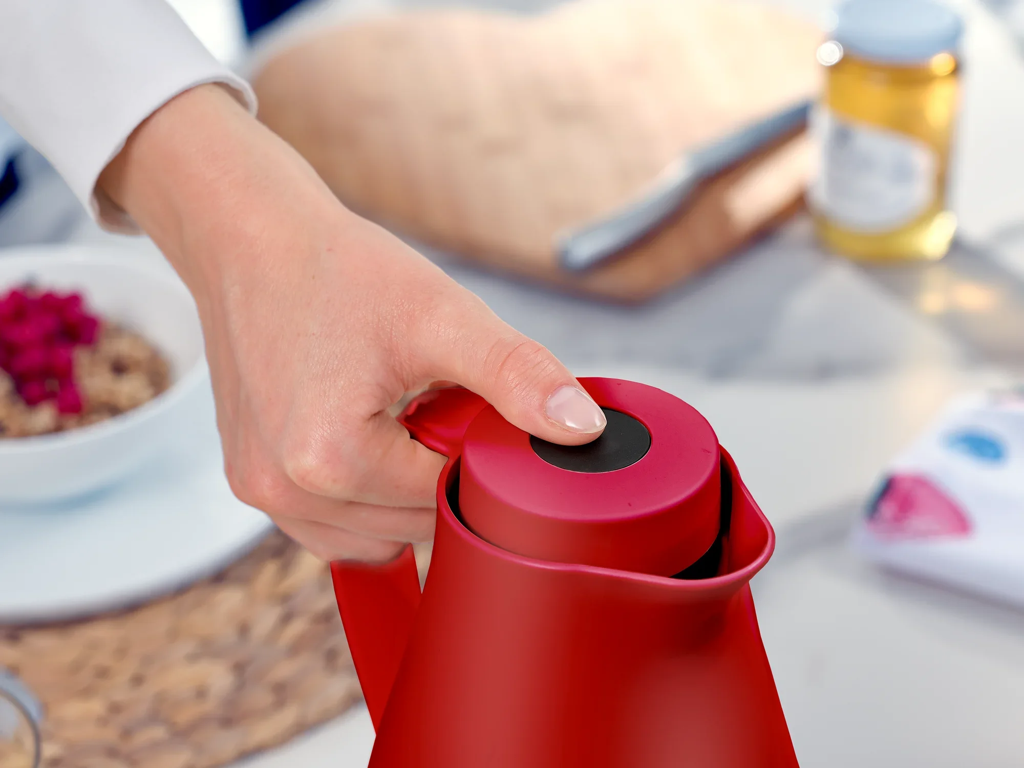 De Harmonic isoleerkan in rood kan met één hand worden geopend. Op de achtergrond is een ontbijttafel met muesli en honing te zien. Ideaal voor stijlvolle warme dranken.