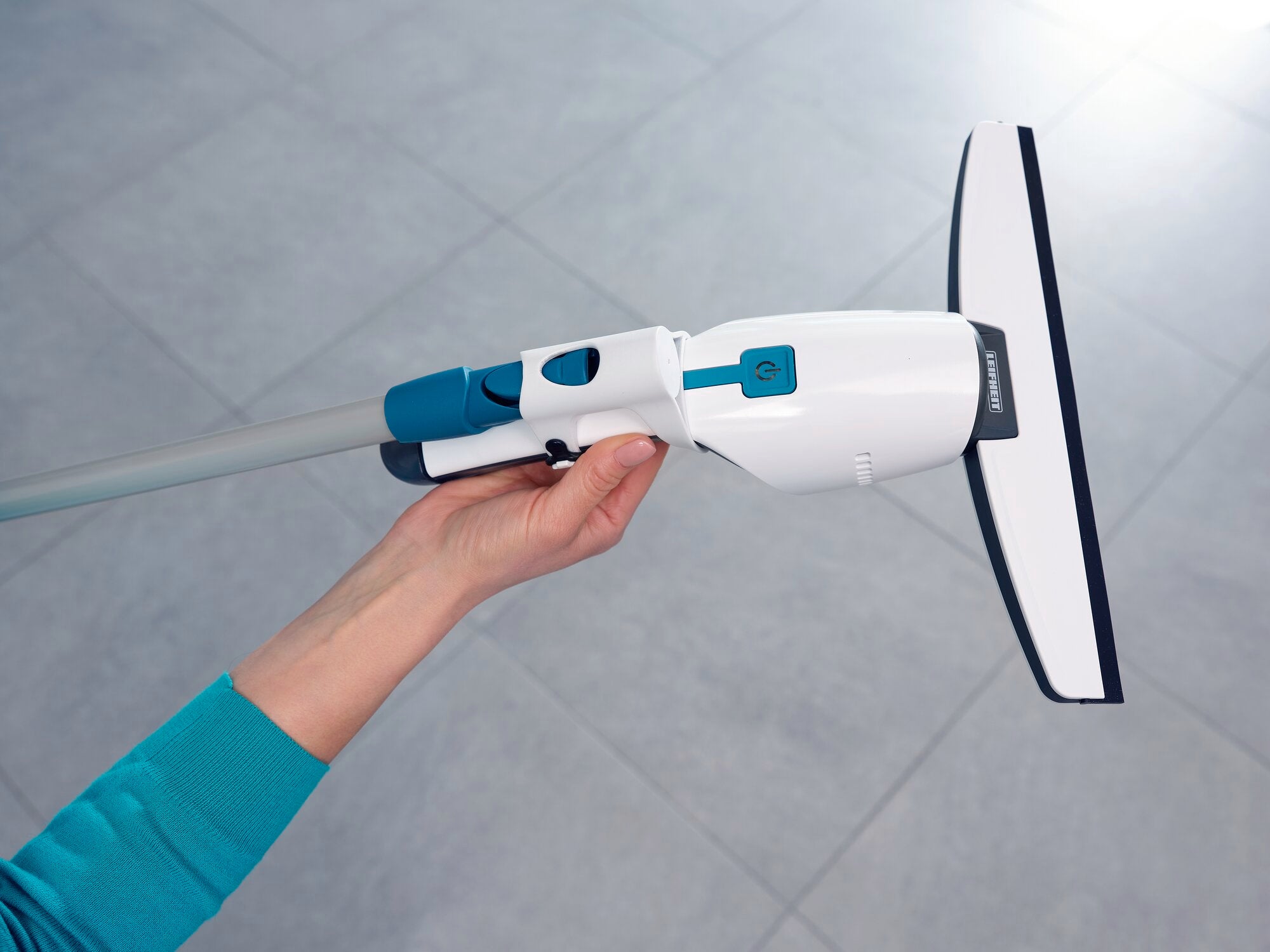 Jedna osoba trzyma odkurzacz do okien Nemo, który został opracowany do czyszczenia okien i łazienek. Odkurzacz jest biały z niebieskimi akcentami i ma szeroką gumową krawędź.