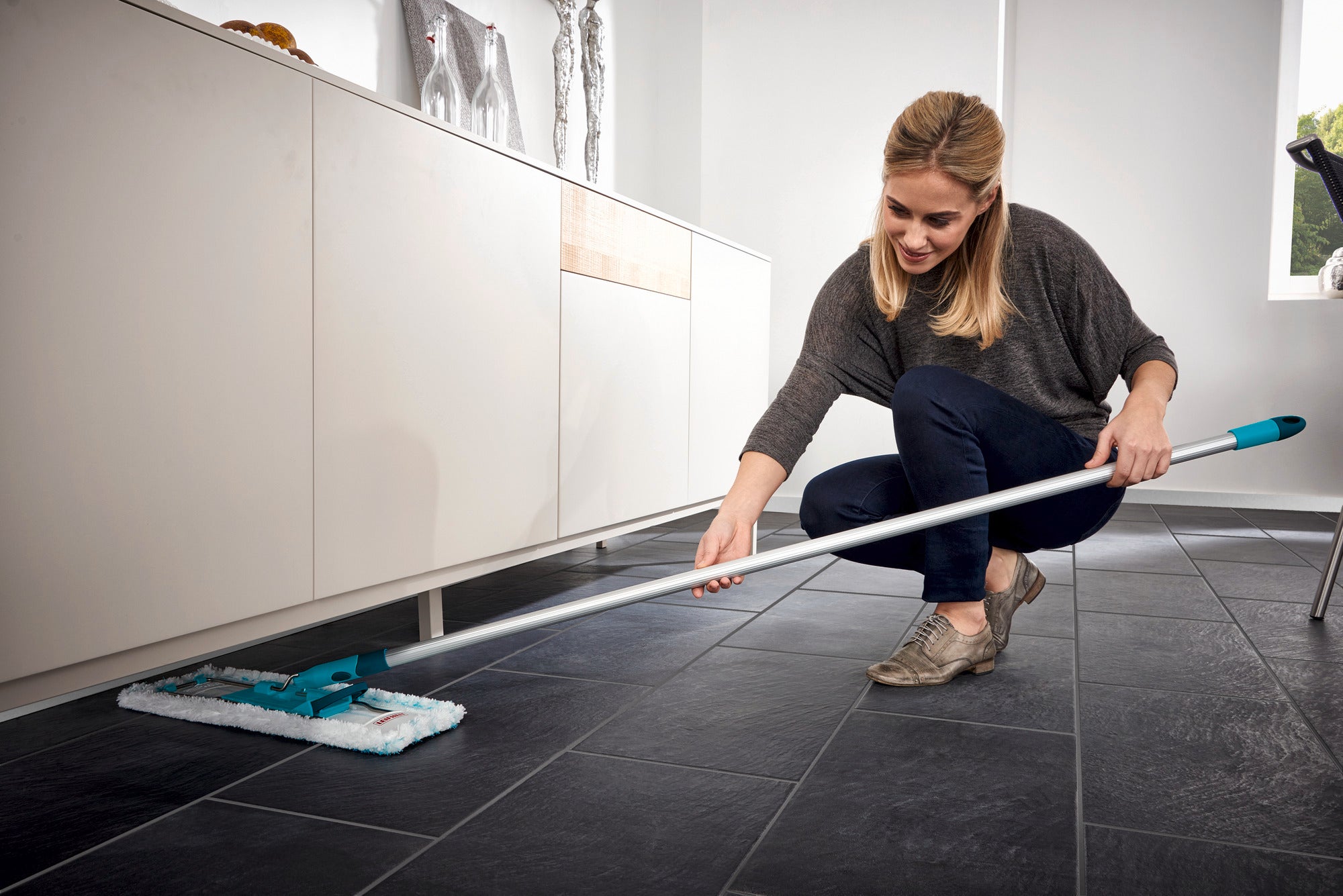 Eine Frau reinigt den Boden mit dem Bodenwischer Profi XL. Der Wischer hat einen langen Stiel und ein rechteckiges Wischtuch, ideal für große Flächen.