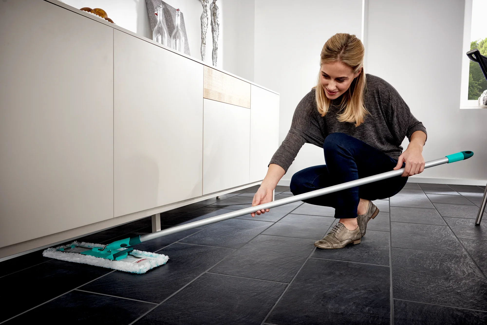 Een vrouw dweilt de vloer met de Profi XL dweilmop. De mop heeft een lange steel en een rechthoekige mopdoek, ideaal voor grote oppervlakken.