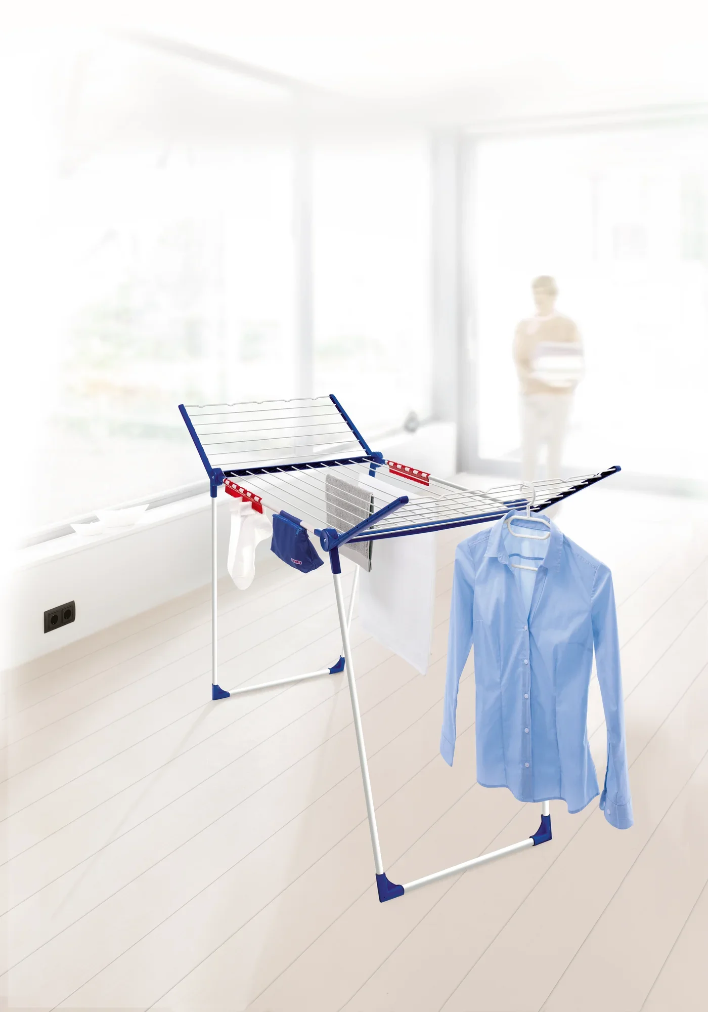 Een vrijstaande wasdroger Pegasus 200 Solid Comfort staat in een lichte ruimte. Het biedt veel ruimte voor het drogen van kleding, waaronder een blauw overhemd en handdoeken.