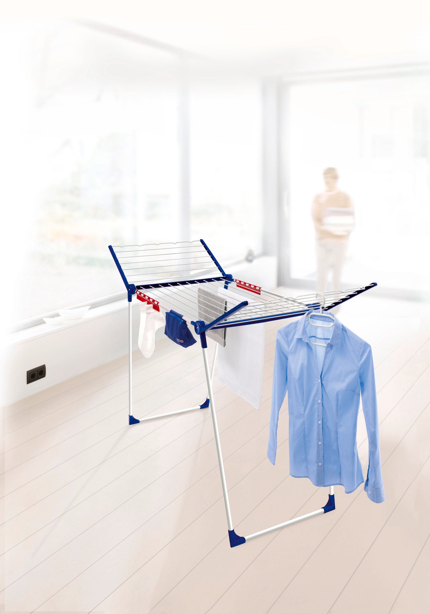 Een vrijstaande wasdroger Pegasus 200 Solid Comfort staat in een lichte ruimte. Het biedt veel ruimte voor het drogen van kleding, waaronder een blauw overhemd en handdoeken.