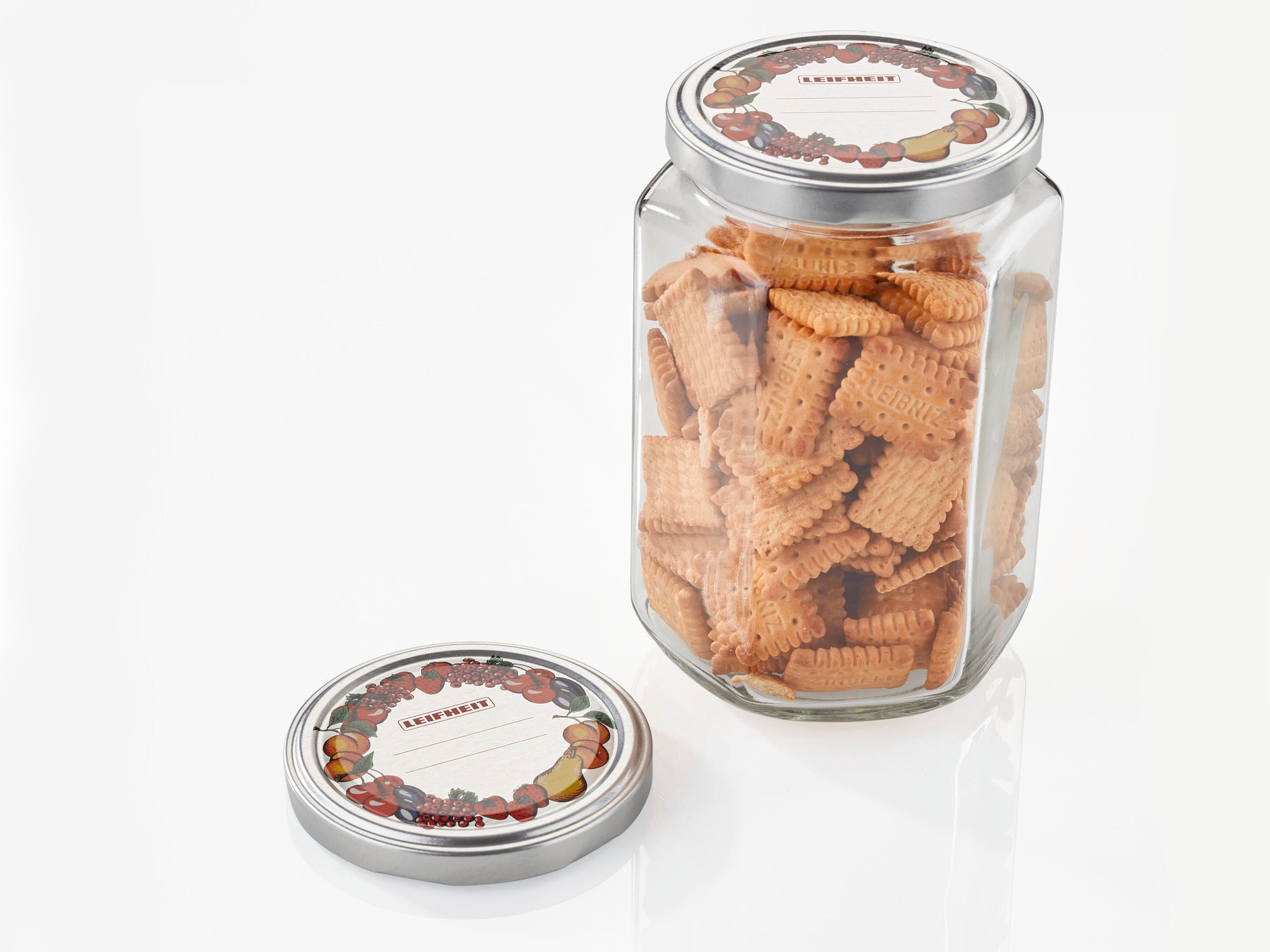 Een pot met koekjes en een verwijderd vervangend deksel met een diameter van 82 mm. Het deksel heeft een decoratief fruitmotief. Ideaal voor het bewaren van gebak.