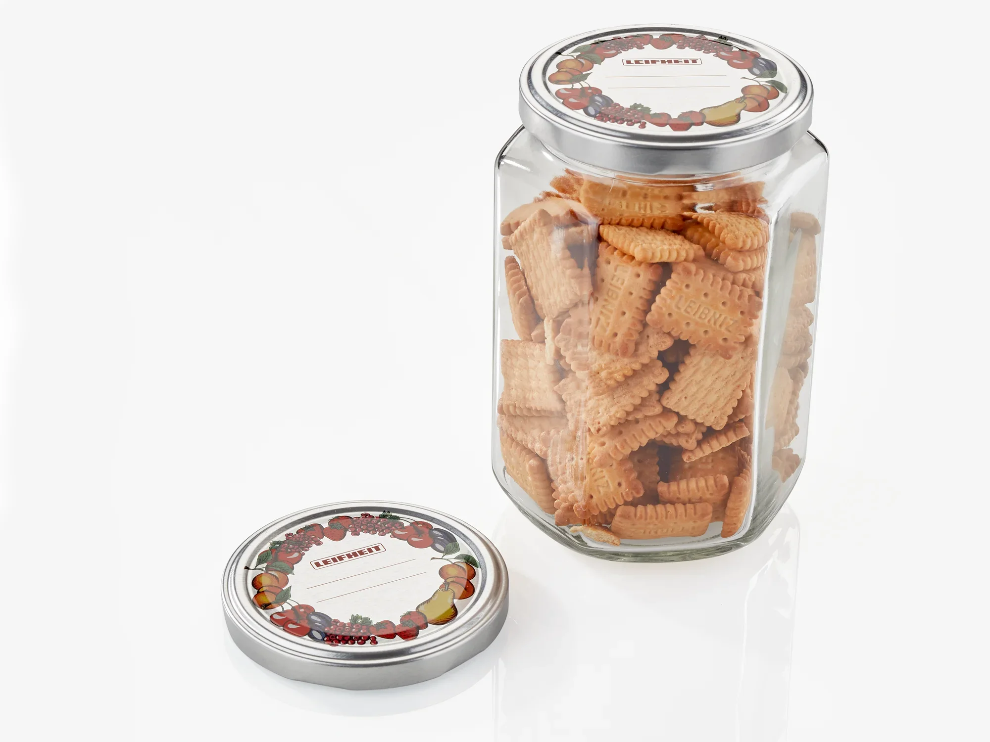 Słoik z herbatnikami i zdjętą pokrywką o średnicy 82 mm. Na pokrywce znajduje się dekoracyjny wzór owoców. Idealny do przechowywania wypieków.